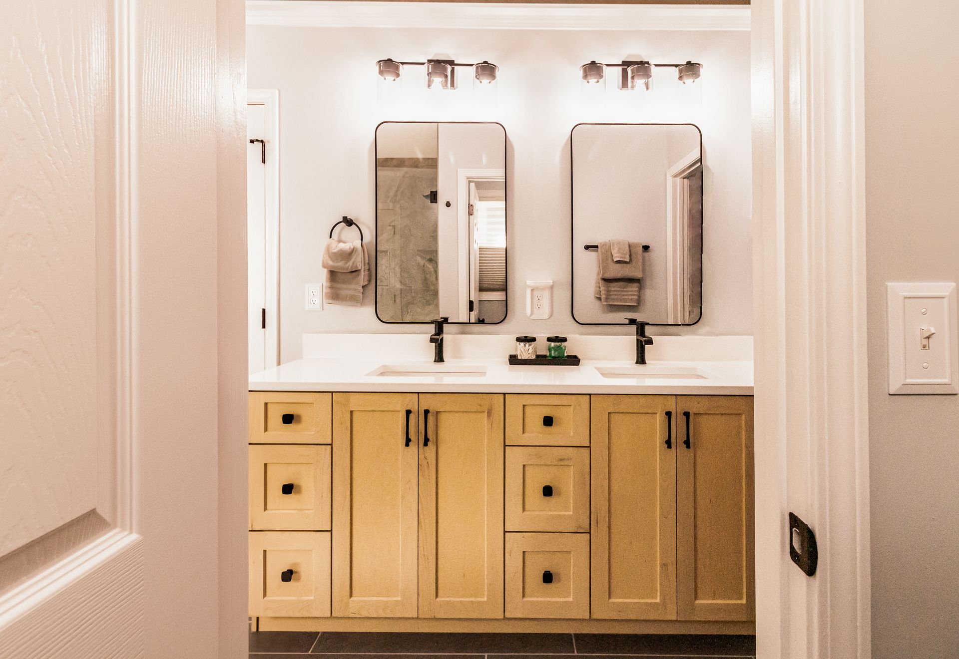 Bathroom vanity with two mirrors, light wood cabinets, and white countertops in a doorway view