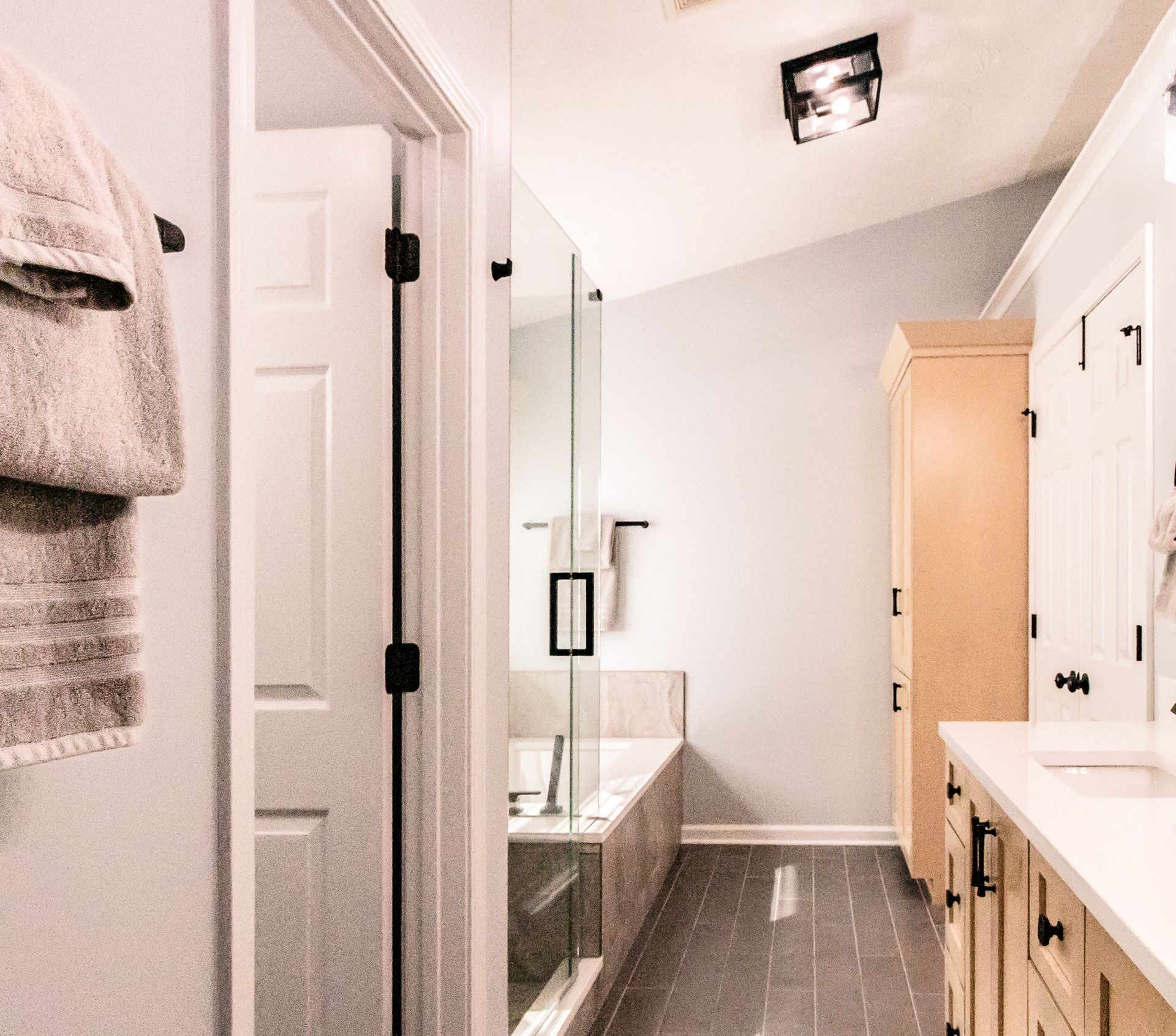 Modern bathroom with glass shower, vanity, white cabinets, and a narrow gray-tiled floor