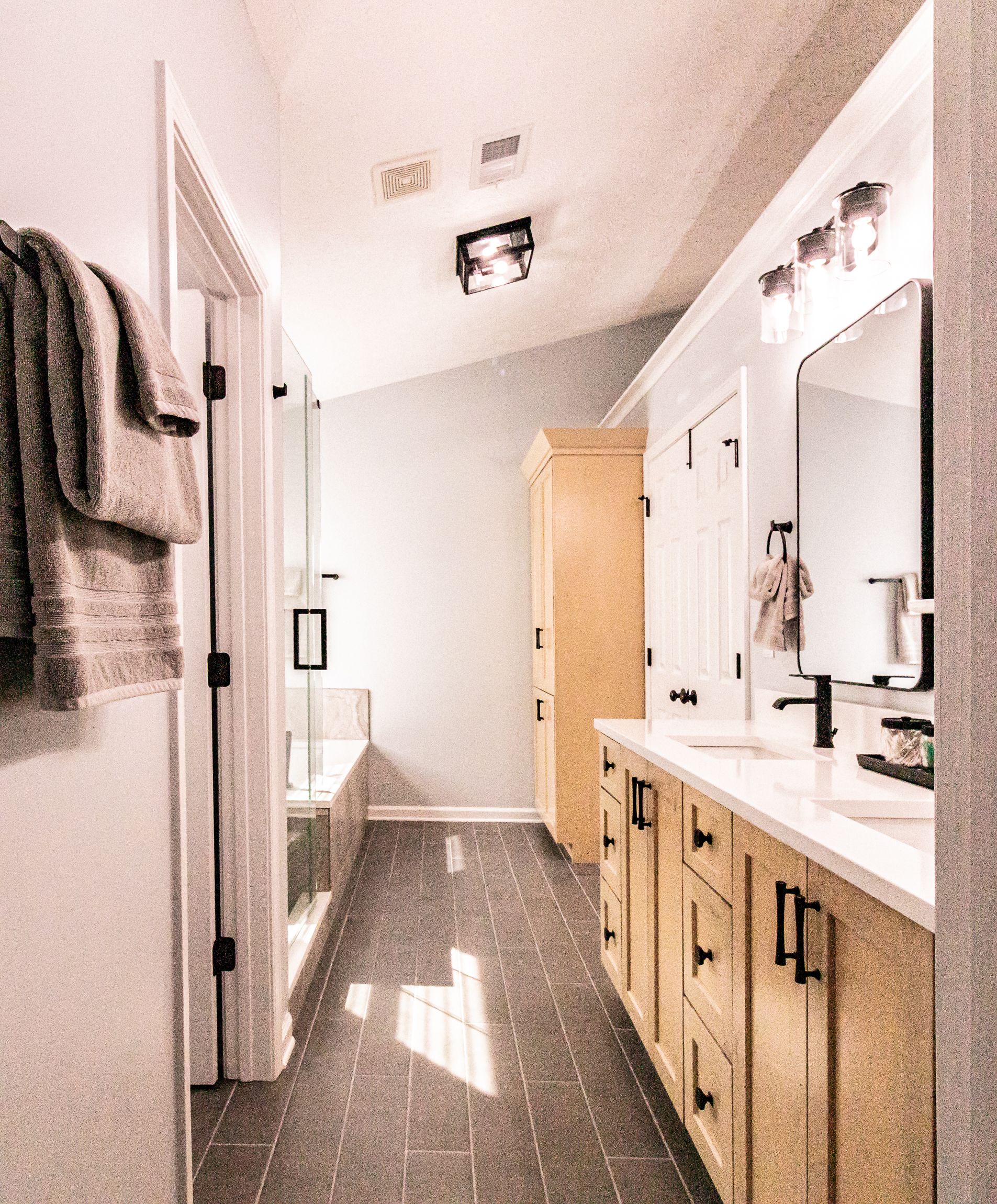 Bright bathroom with double vanity, wood cabinets, large mirror, and a doorway at the back