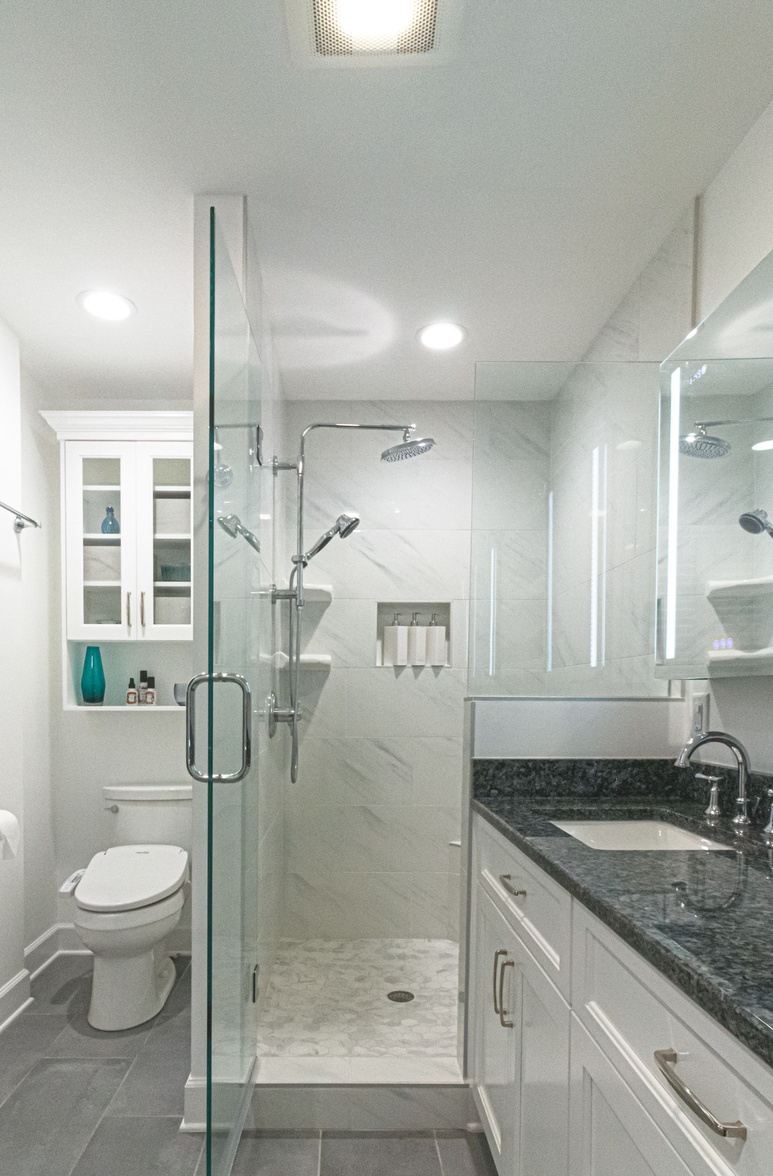 Bright modern bathroom with glass shower, toilet, vanity, and granite countertop
