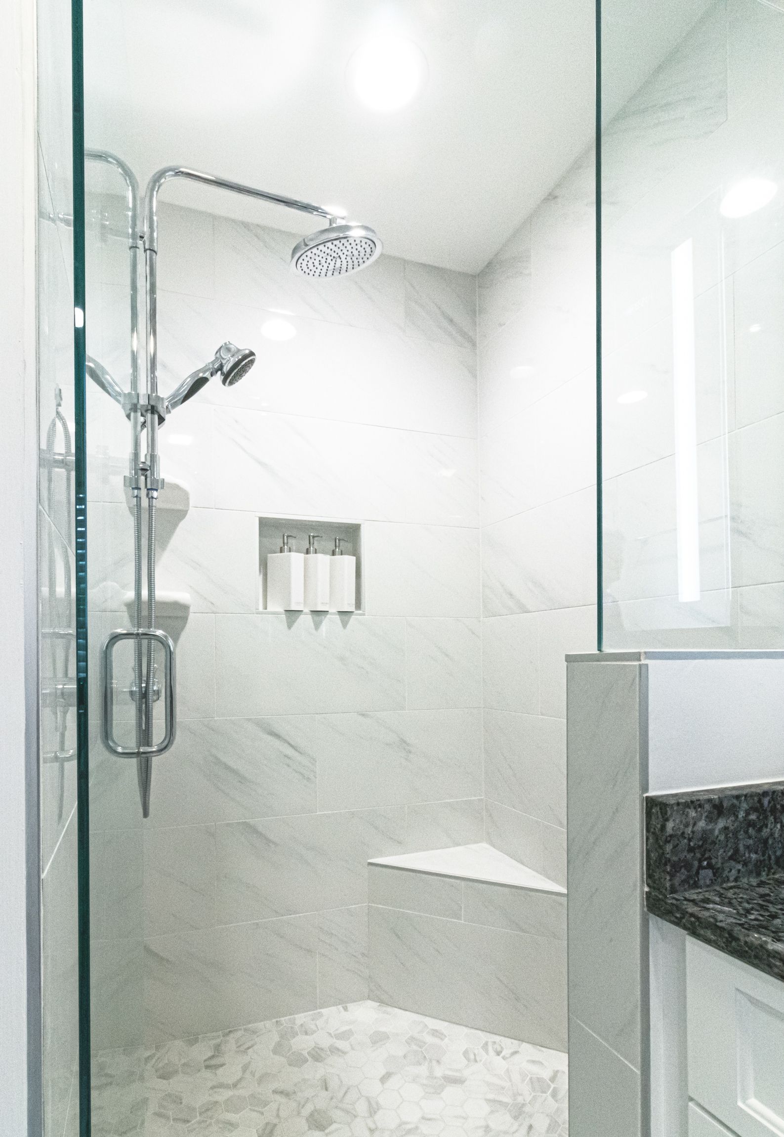 Modern white bathroom shower with glass enclosure, rainfall showerhead, and marble accents