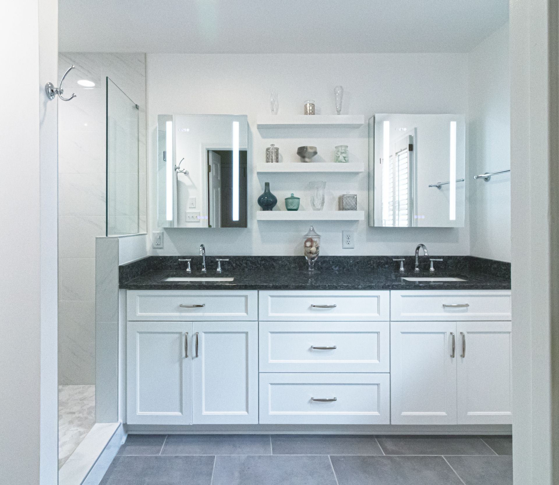 Bright white bathroom with double sinks, black countertop, and mirrored cabinets on tiled floor.
