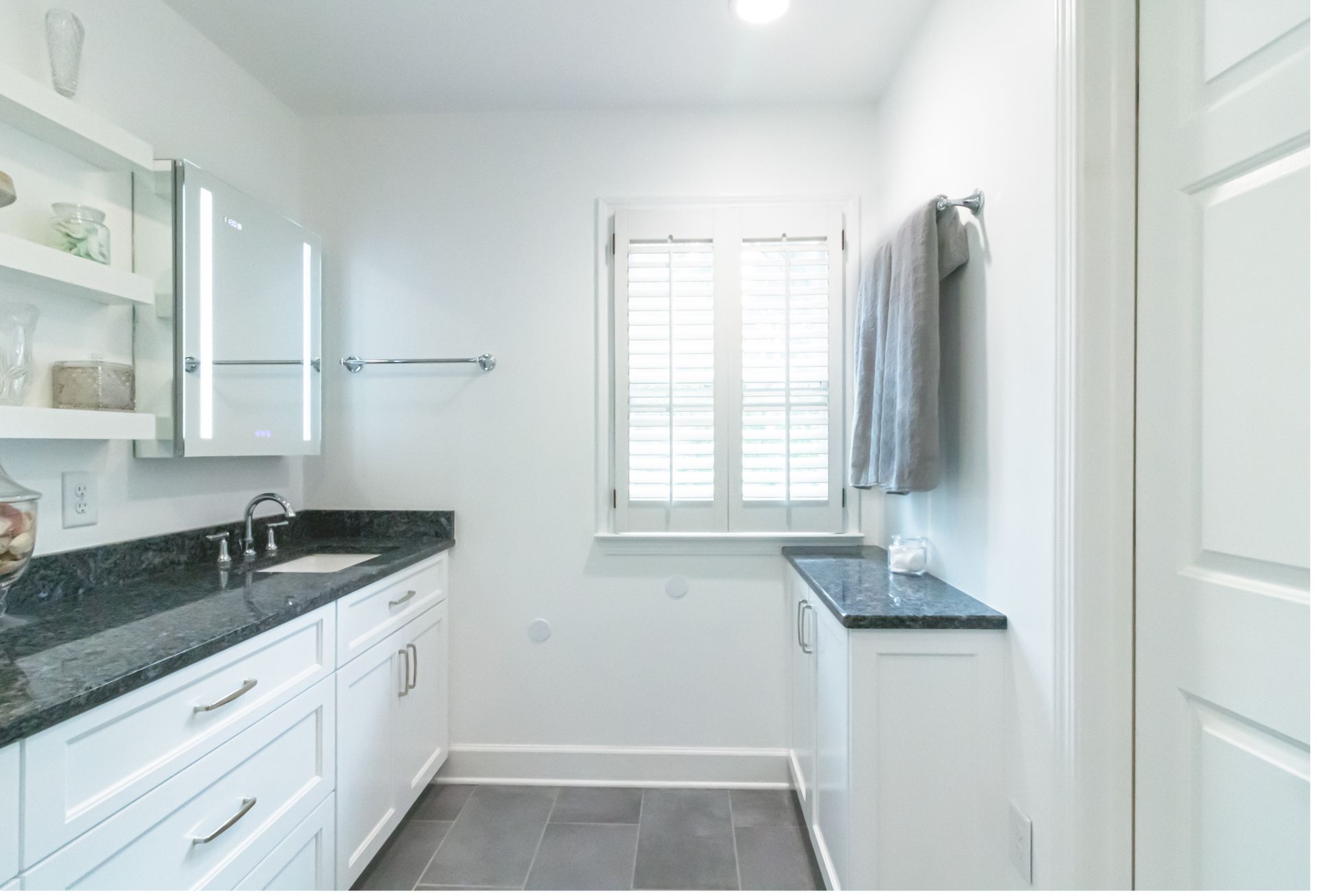 Bright white bathroom with double vanity, black countertop, window, and shower curtain.