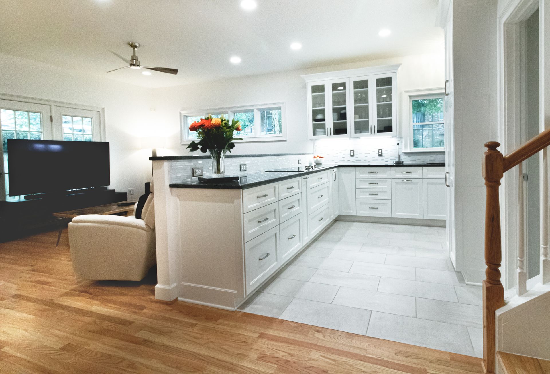 Bright modern kitchen and living area with white cabinets, black island, wood floors, and a TV on the left