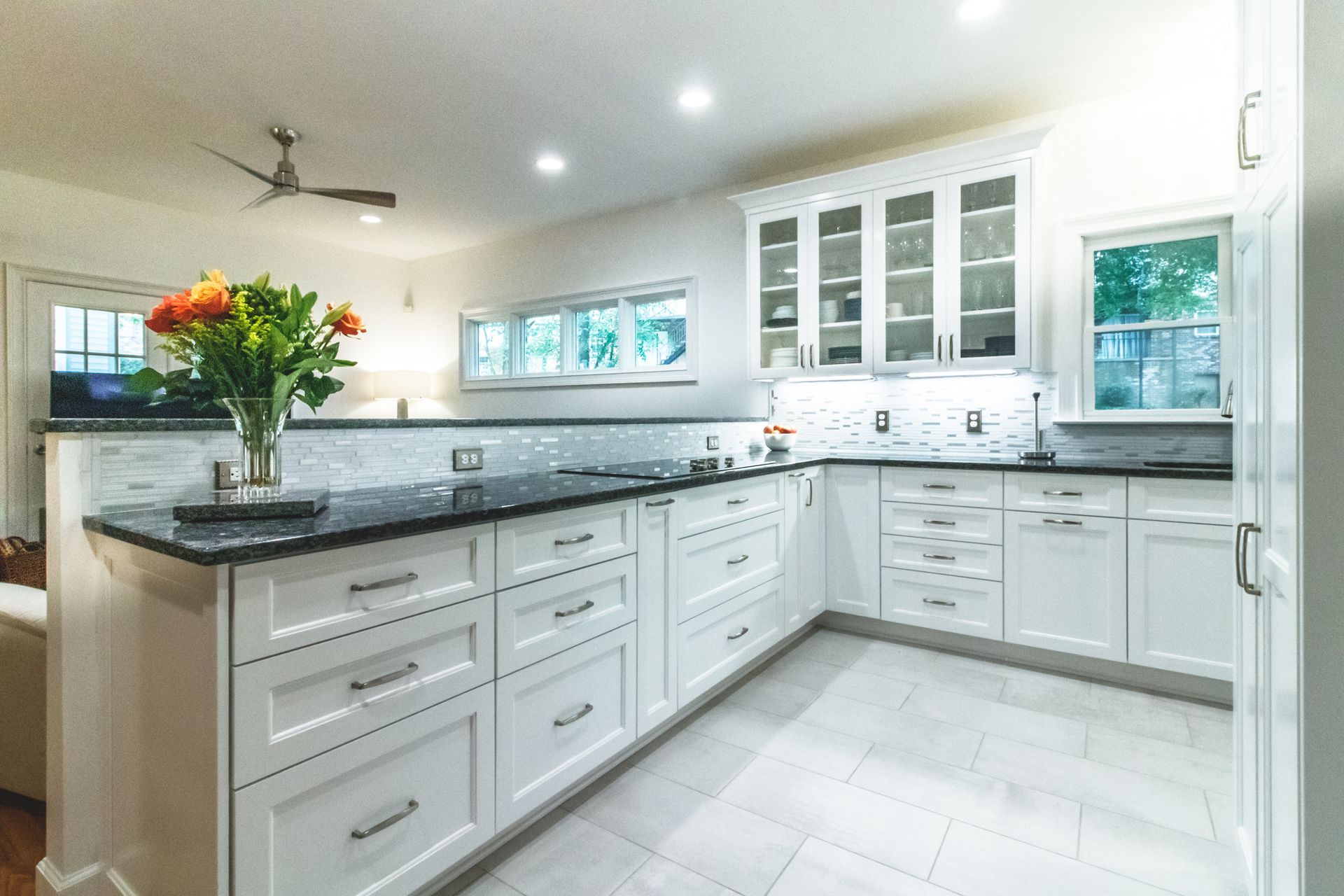 Bright modern white kitchen with island, dark countertops, and a vase of flowers by the sink.