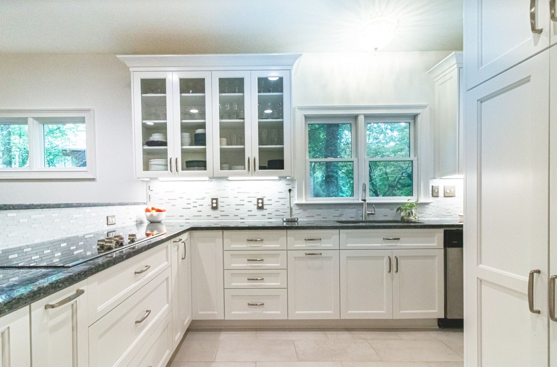 Bright modern white kitchen with black countertops, cabinets, and windows over the sink