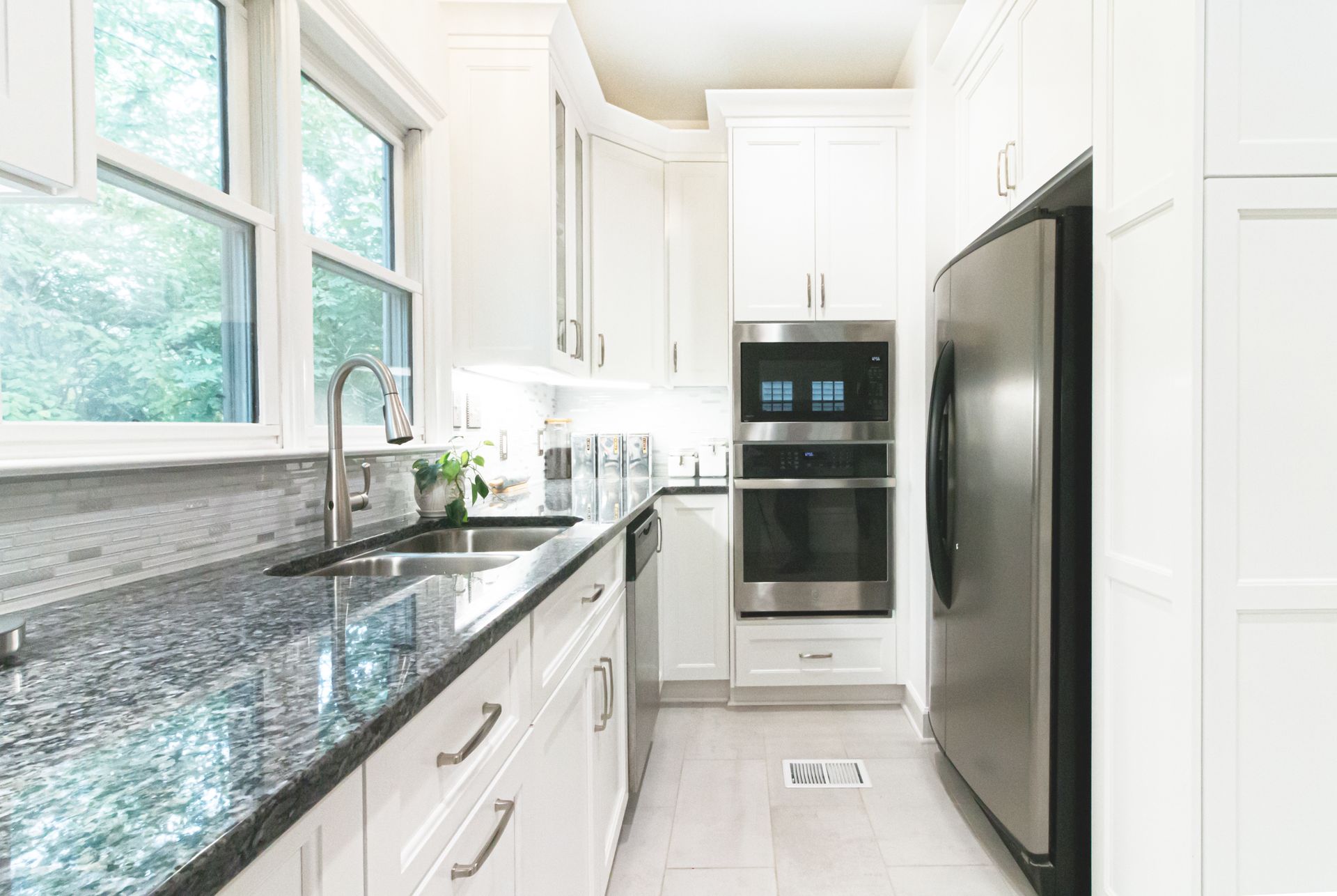 Bright white kitchen with granite countertops, large window, and stainless steel appliances