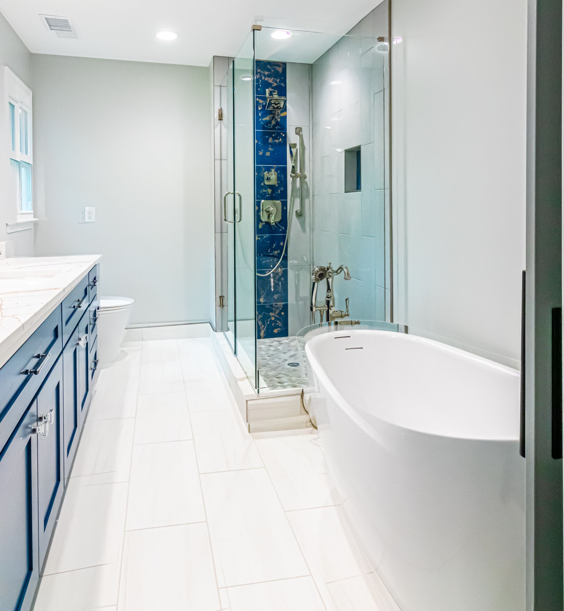 Bright modern bathroom with white tub, glass shower, blue-tiled accent, and blue vanity cabinets