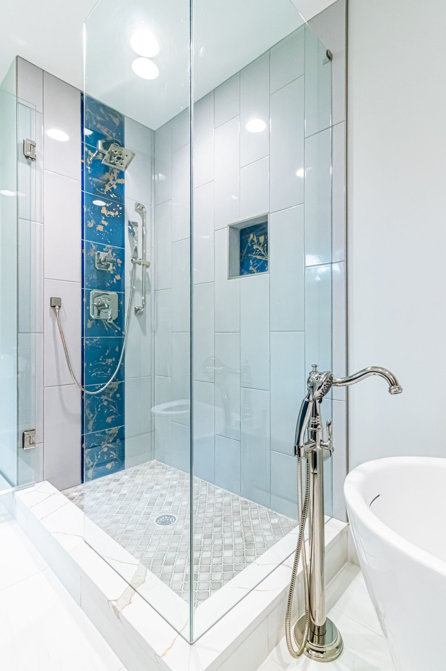 Modern bathroom with glass shower enclosure, blue tile accent, and white tub