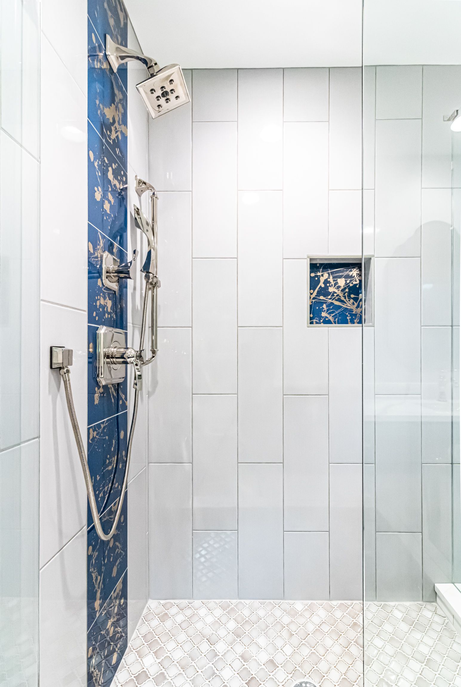 Modern bathroom shower with white and blue tiled walls, glass enclosure, and mosaic floor.
