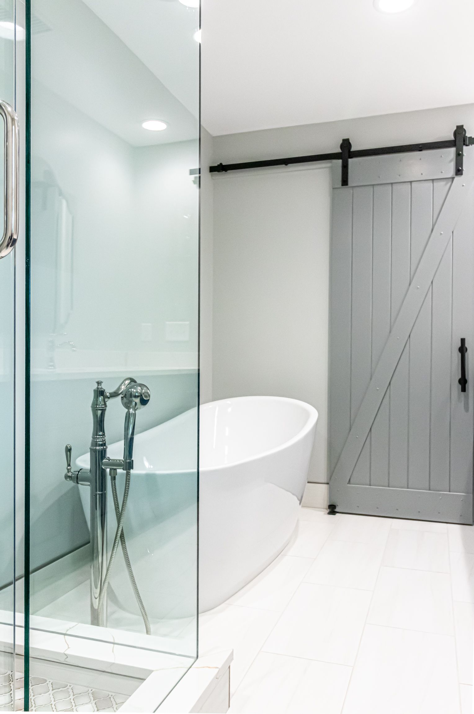 Modern white bathroom with glass shower, freestanding tub, and gray barn-style door