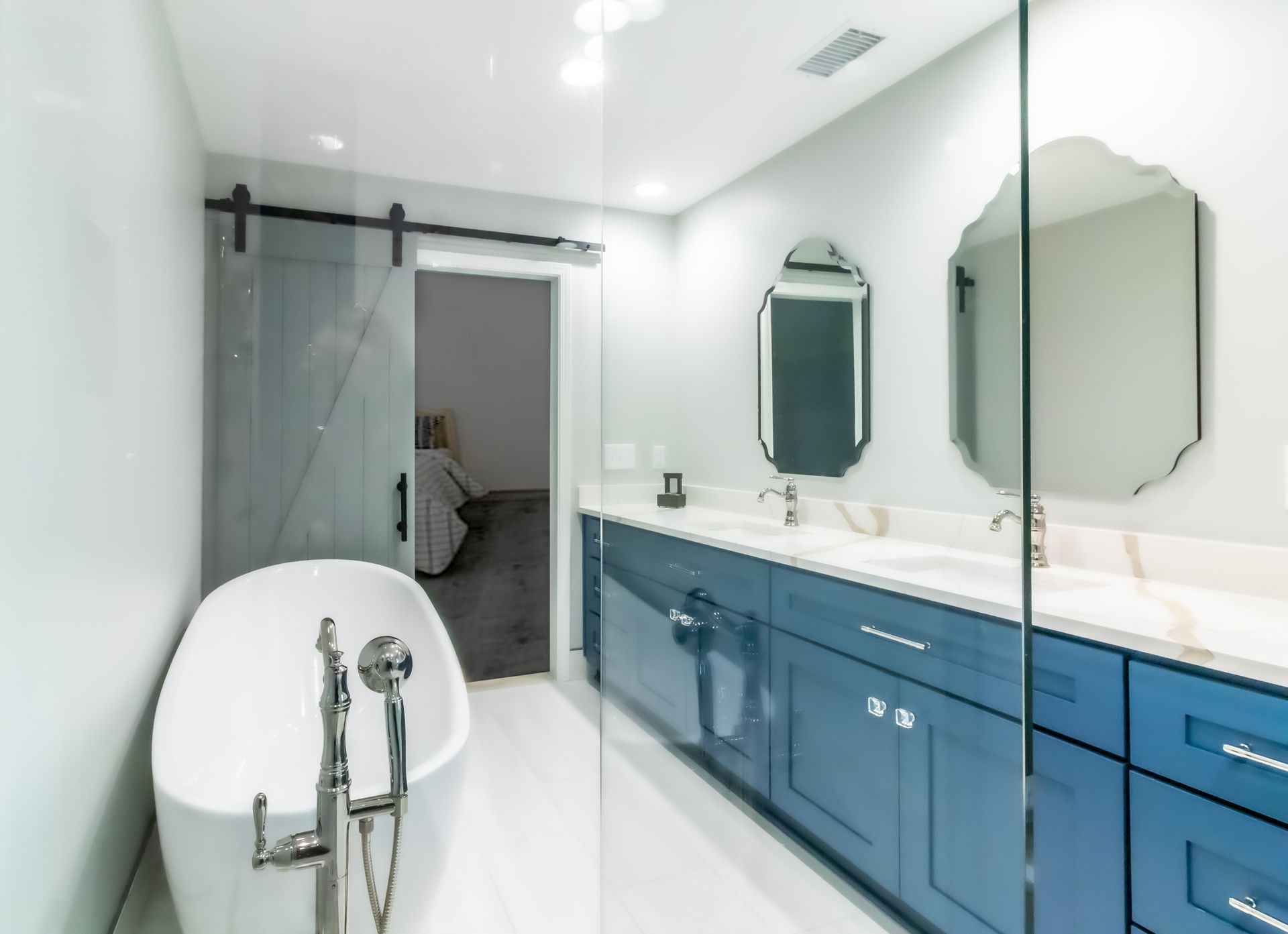 Modern bathroom with glass shower, freestanding tub, and blue vanity along a mirrored wall