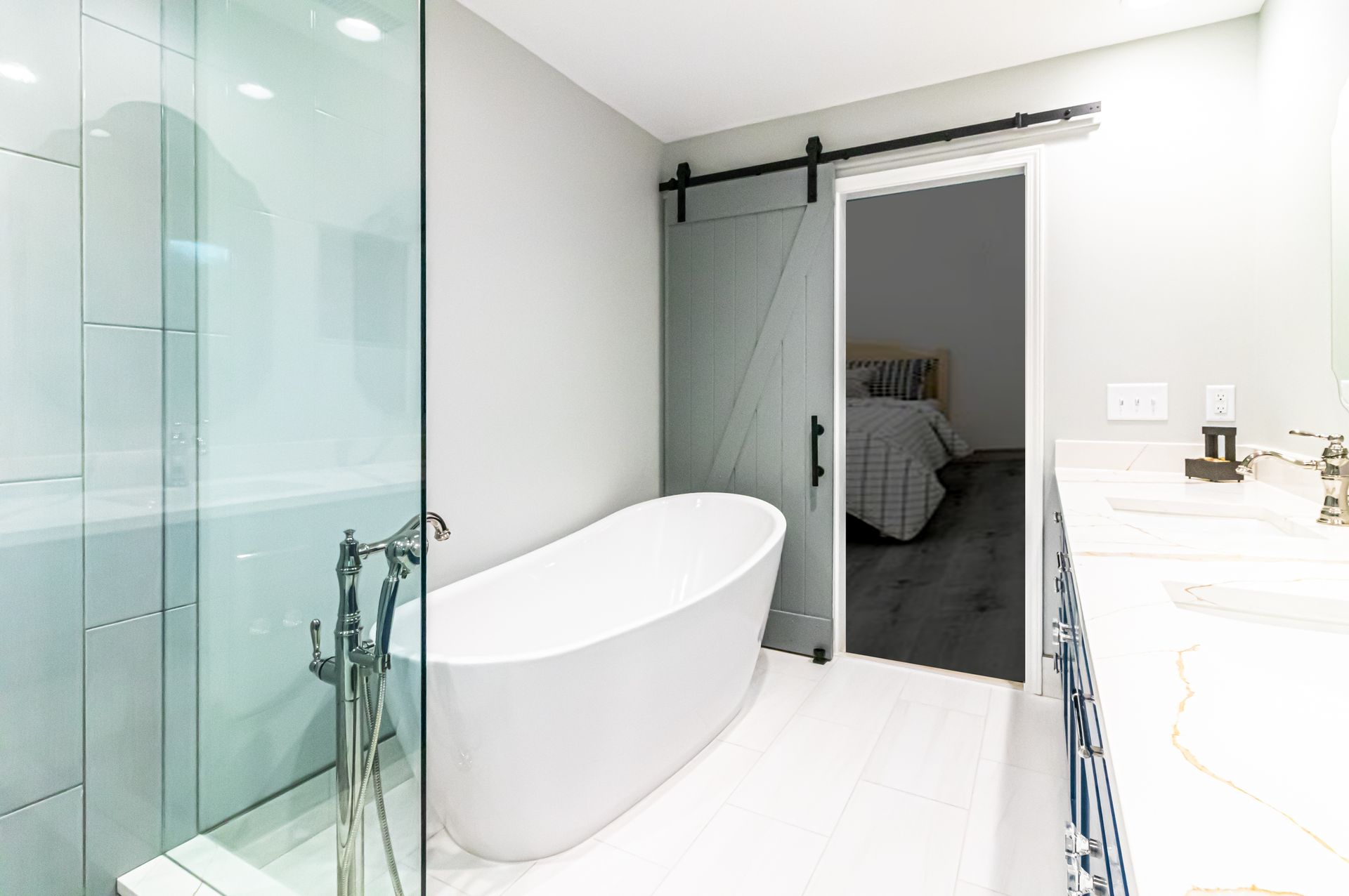 Modern white bathroom with glass shower, freestanding tub, and open doorway to a bedroom