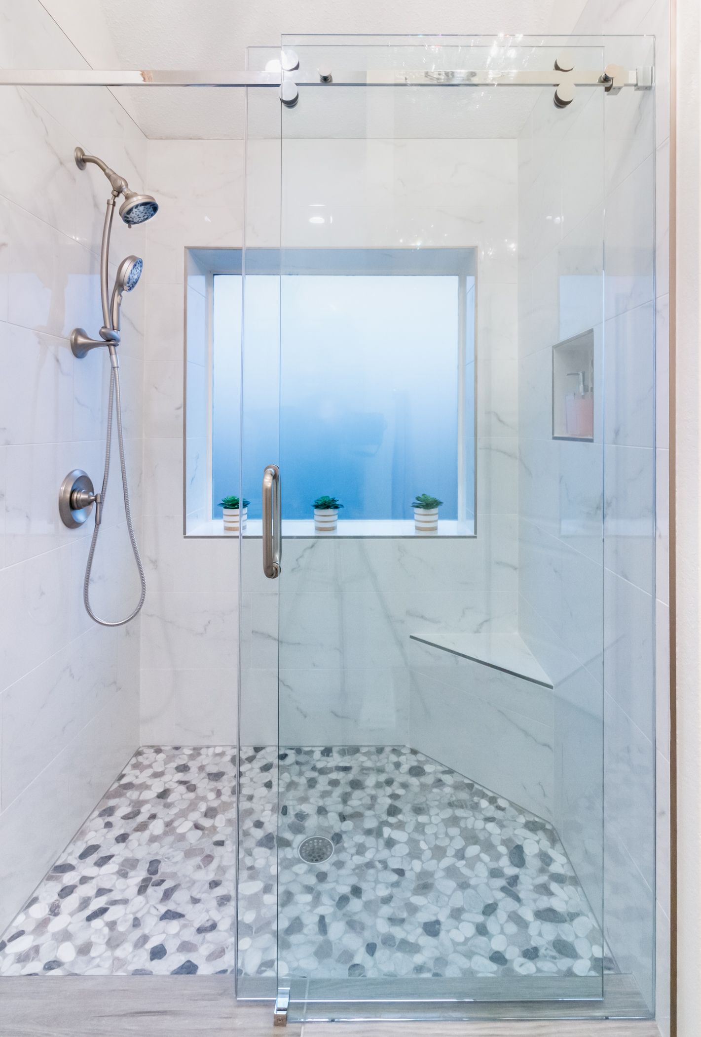 Modern glass shower with pebble tile floor, chrome fixtures, and frosted window.