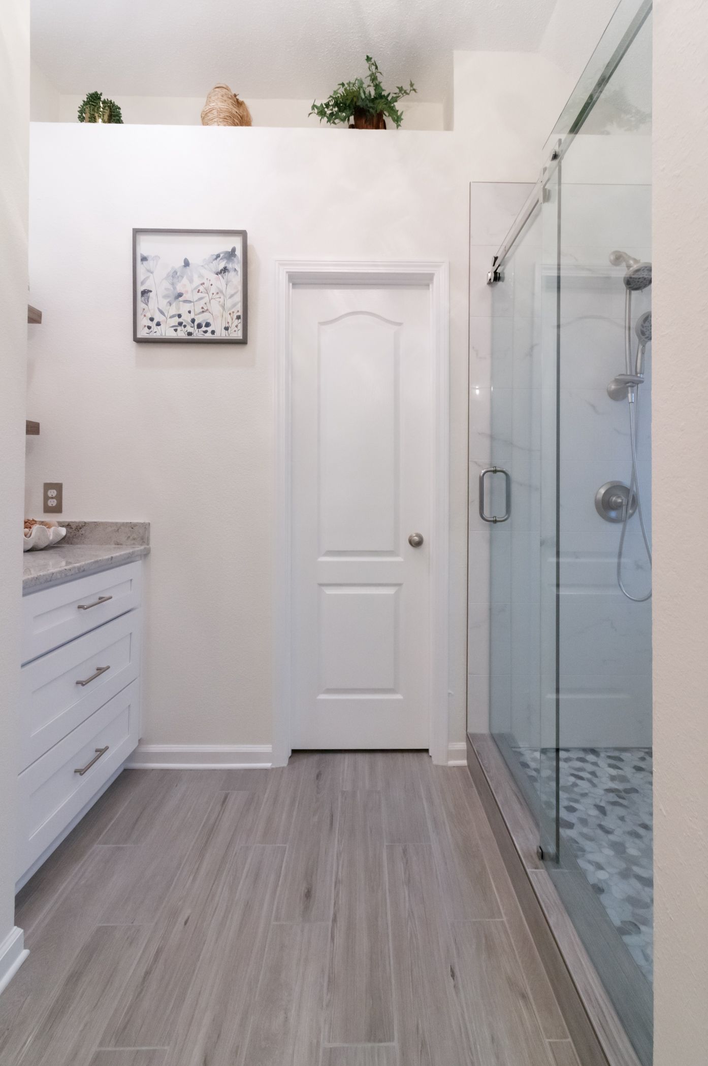 Modern bathroom with white vanity, centered door, and glass-enclosed shower on the right.