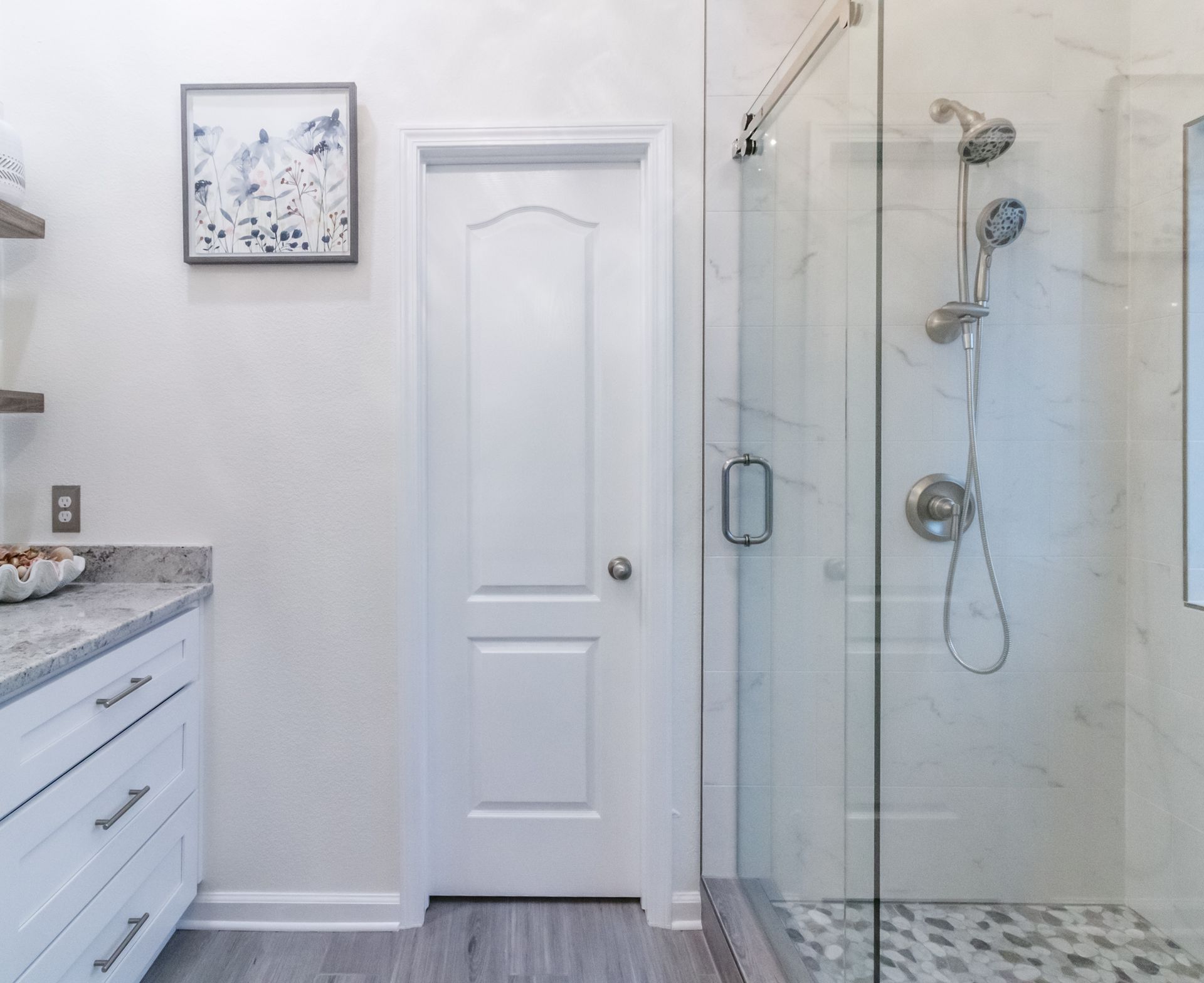 Modern bathroom with white vanity, closed door, and glass shower enclosure with tiled floor.