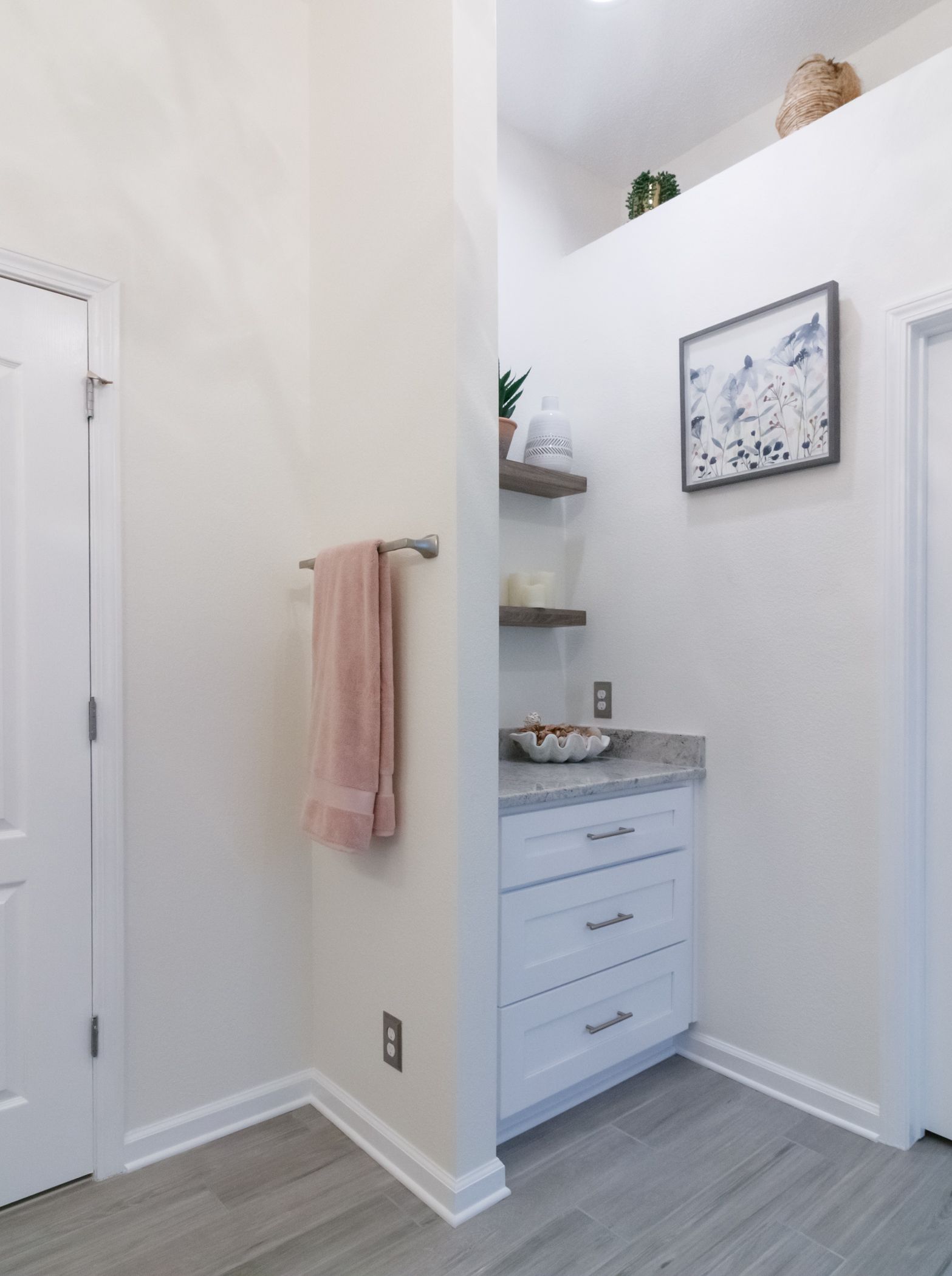 Bright hallway with white walls, towel rack, and a small blue dresser nook with shelves and wall art