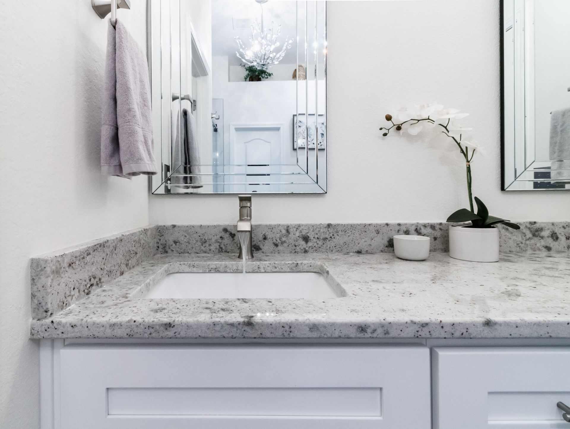 Bright modern bathroom vanity with speckled granite countertop, sink, mirror, towels, and orchid plant.