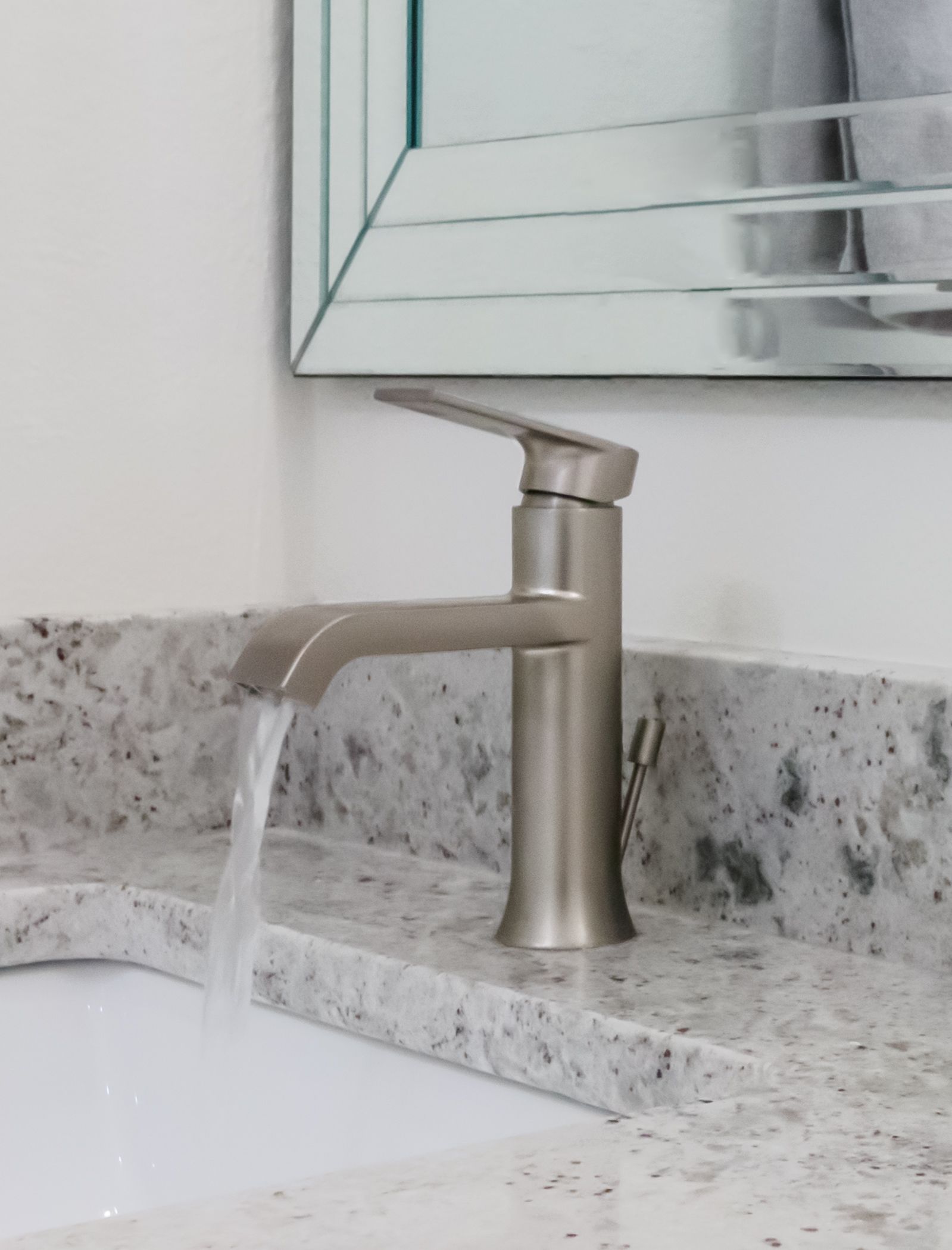 Bathroom faucet with water flowing into a white sink beside a gray stone countertop