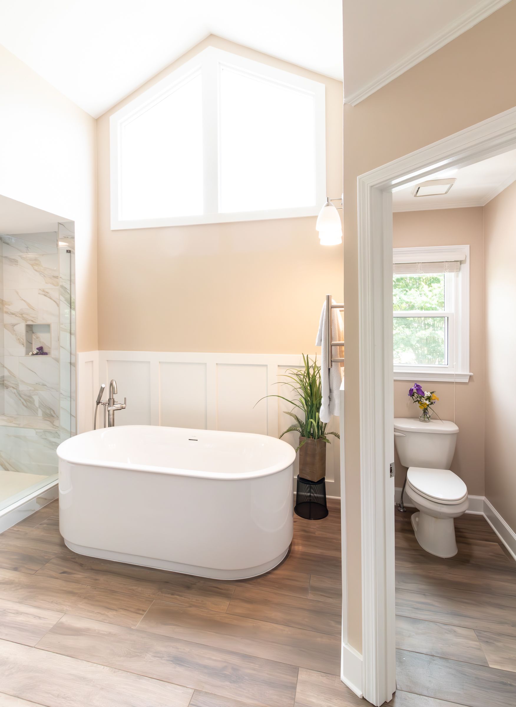 Bright bathroom with freestanding tub, walk-in shower, and toilet in a light beige and white interior