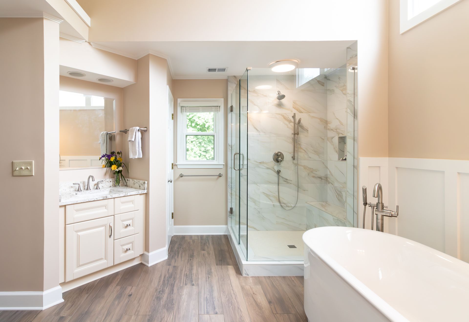 Bright modern bathroom with glass shower, freestanding tub, vanity, and wood-look floor
