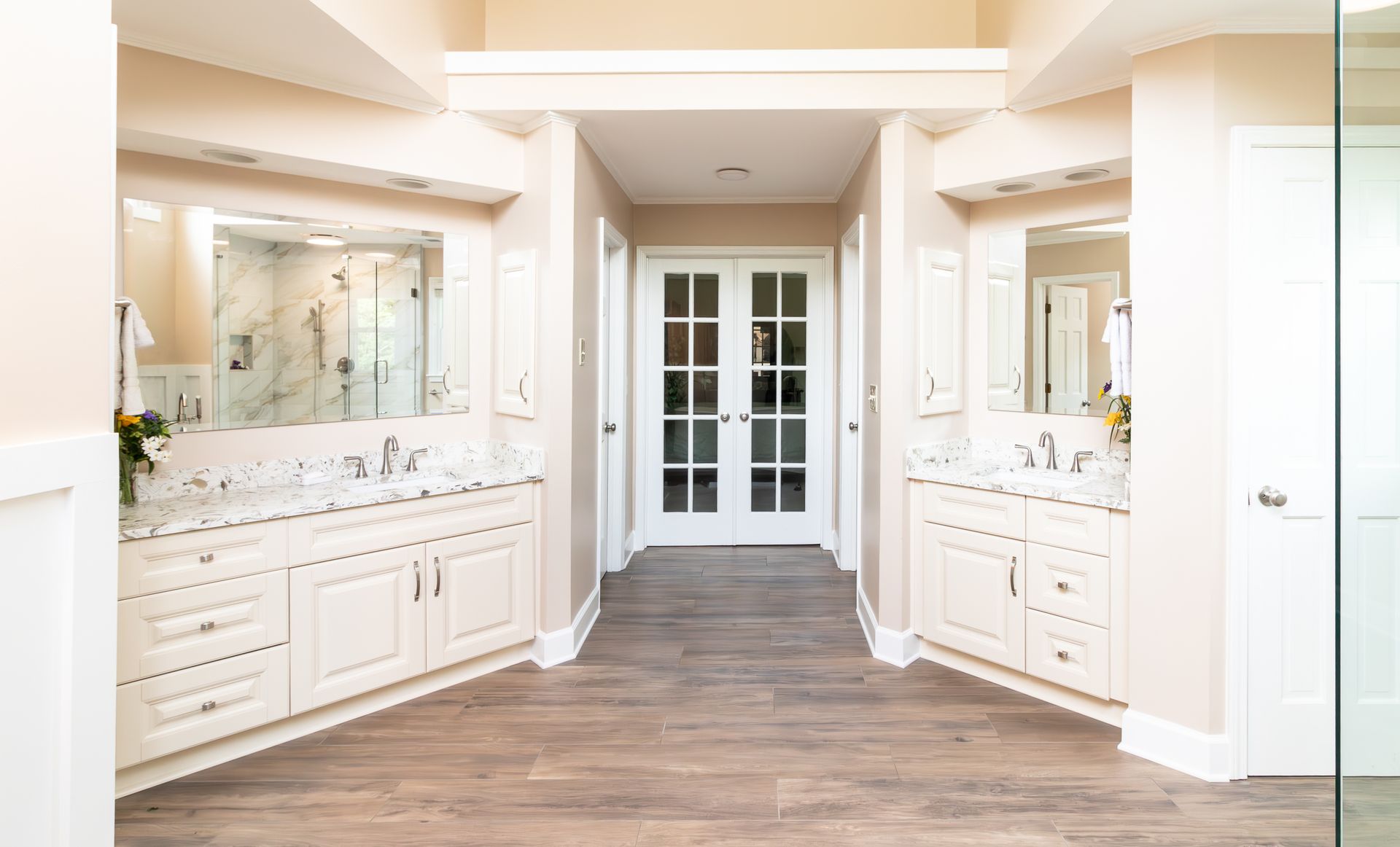 Bright bathroom with double vanities, large mirrors, and French doors at the back.