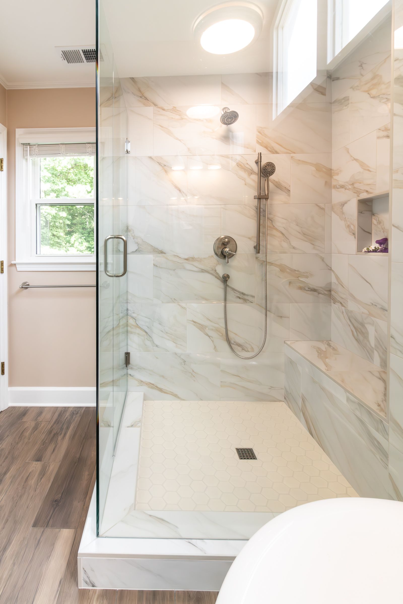 Modern tiled walk-in shower with glass door, built-in bench, and white pebble shower floor