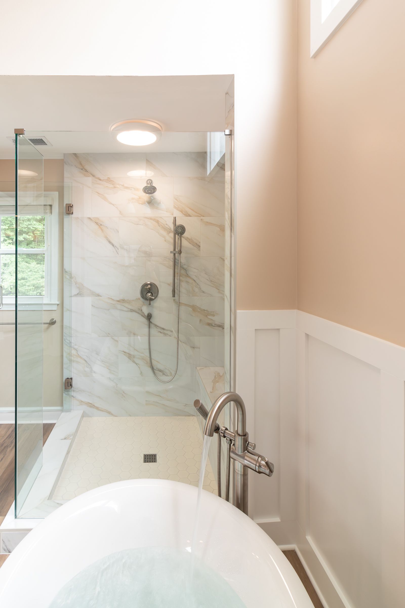 Modern bathroom with glass shower, freestanding tub, and beige walls