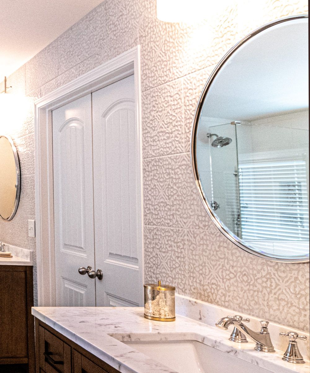 Bathroom vanity with round mirror, white cabinets, and marble countertop beside a closed door.