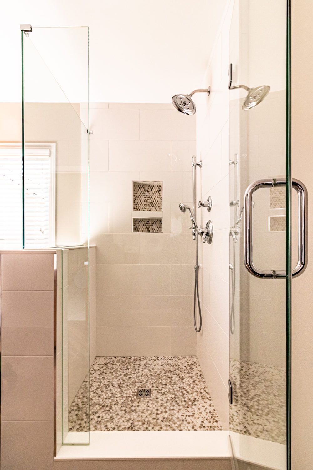 Modern tiled walk-in shower with glass door, chrome fixtures, and pebble floor