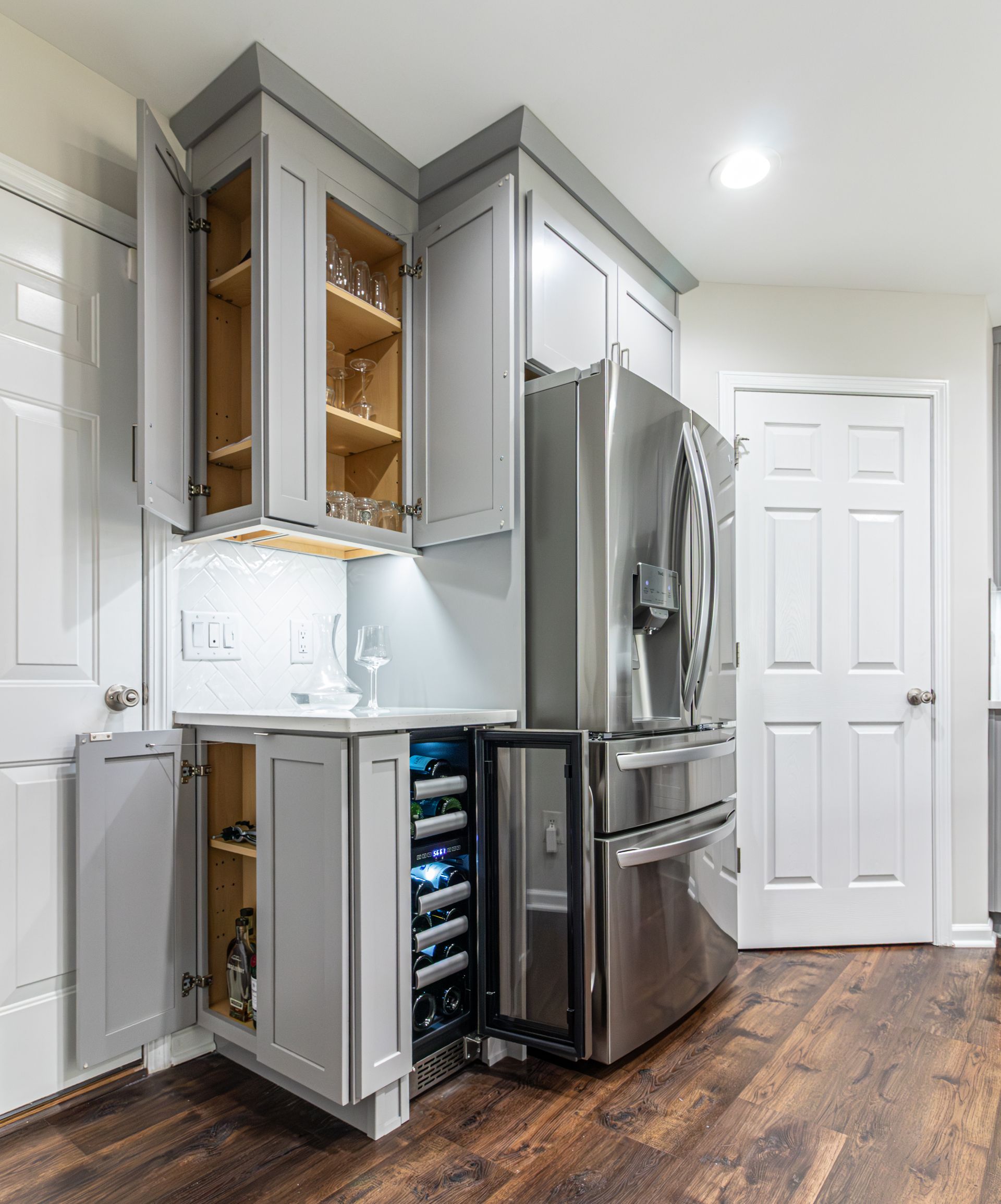 Modern kitchen with gray cabinets, stainless steel refrigerator, and wine cooler under open upper cabinets
