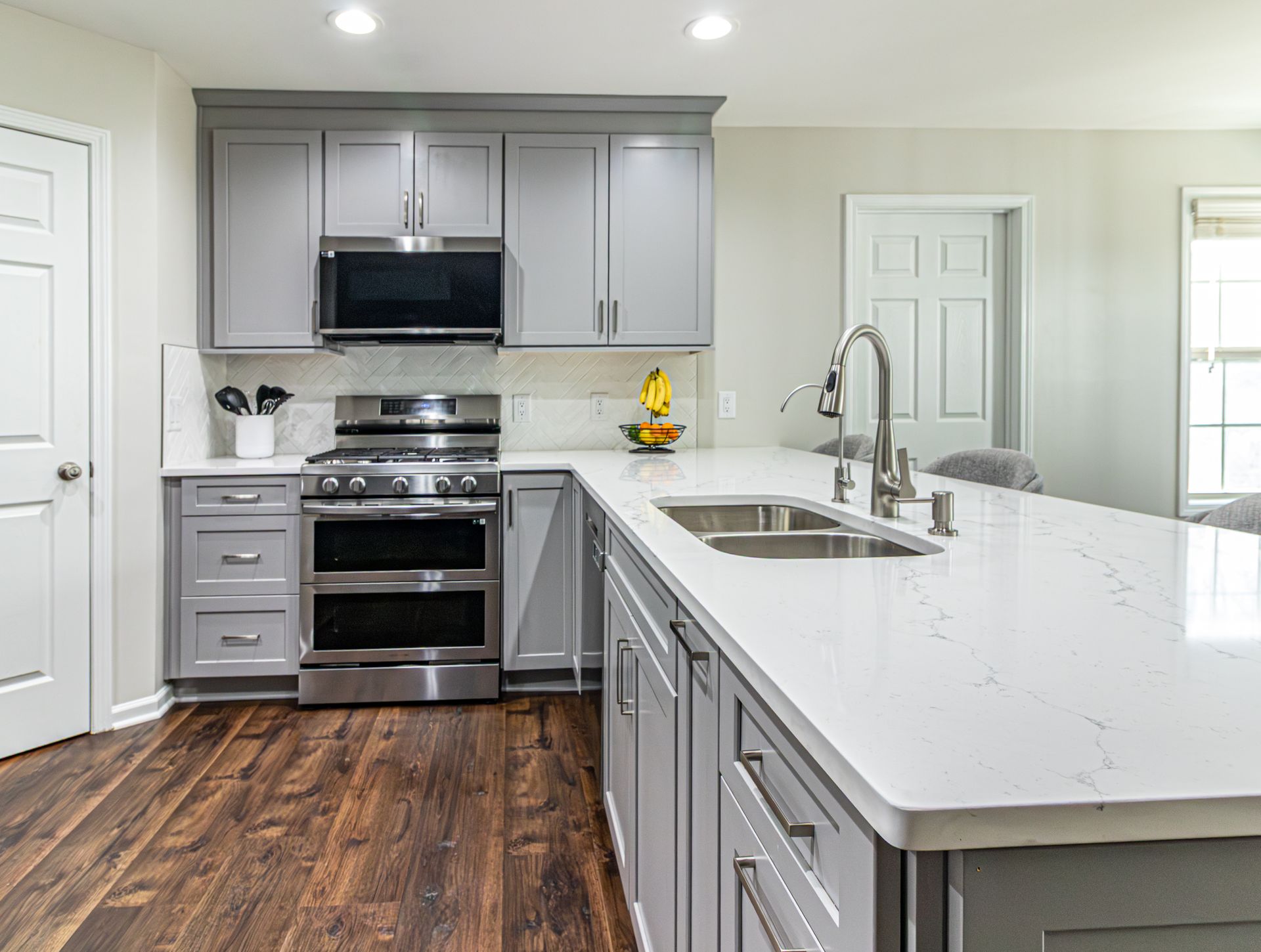 Modern kitchen with gray cabinets, white island, stainless appliances, and dark wood floors