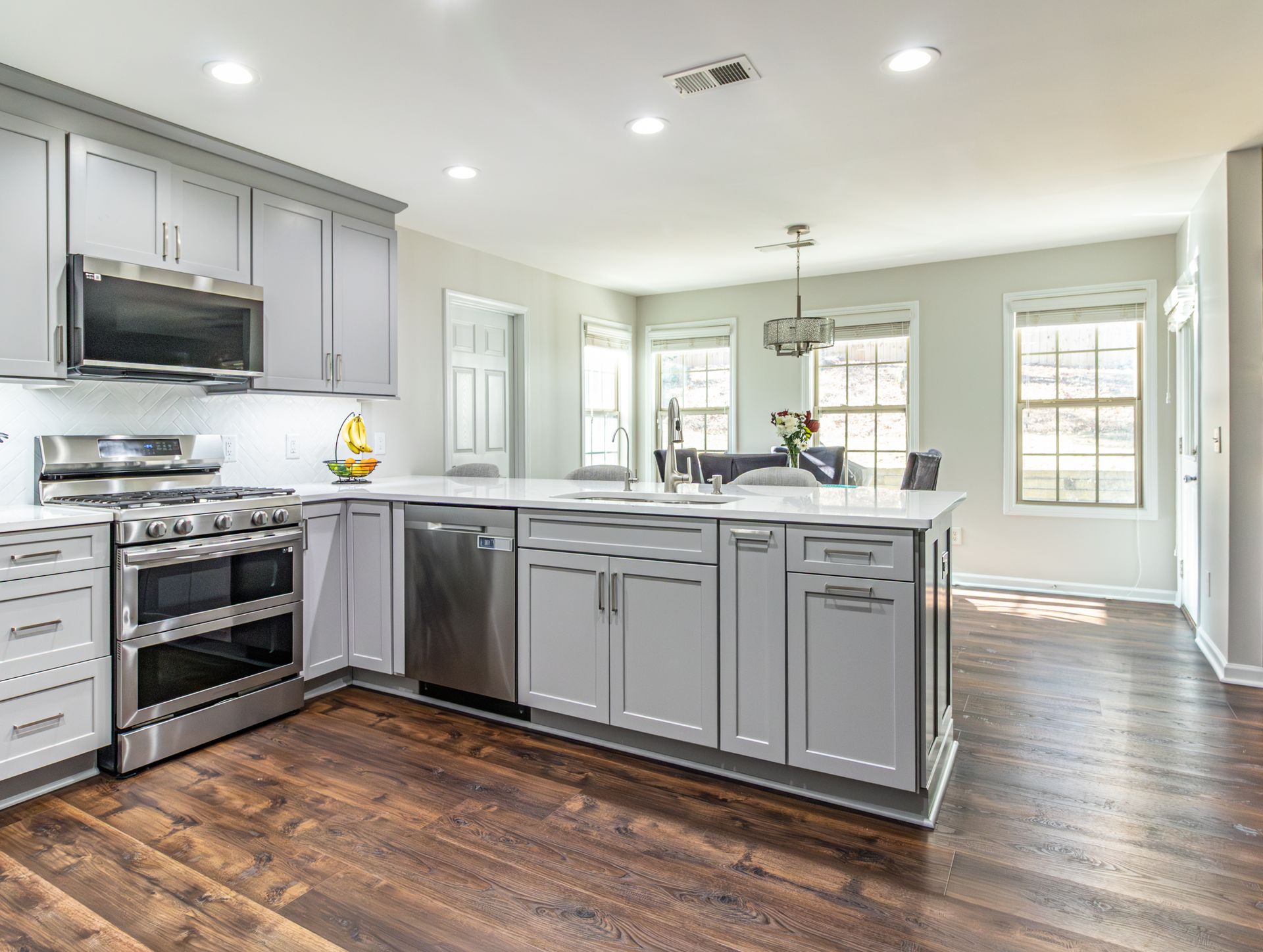Bright modern kitchen with gray cabinets, stainless appliances, island, and hardwood floors