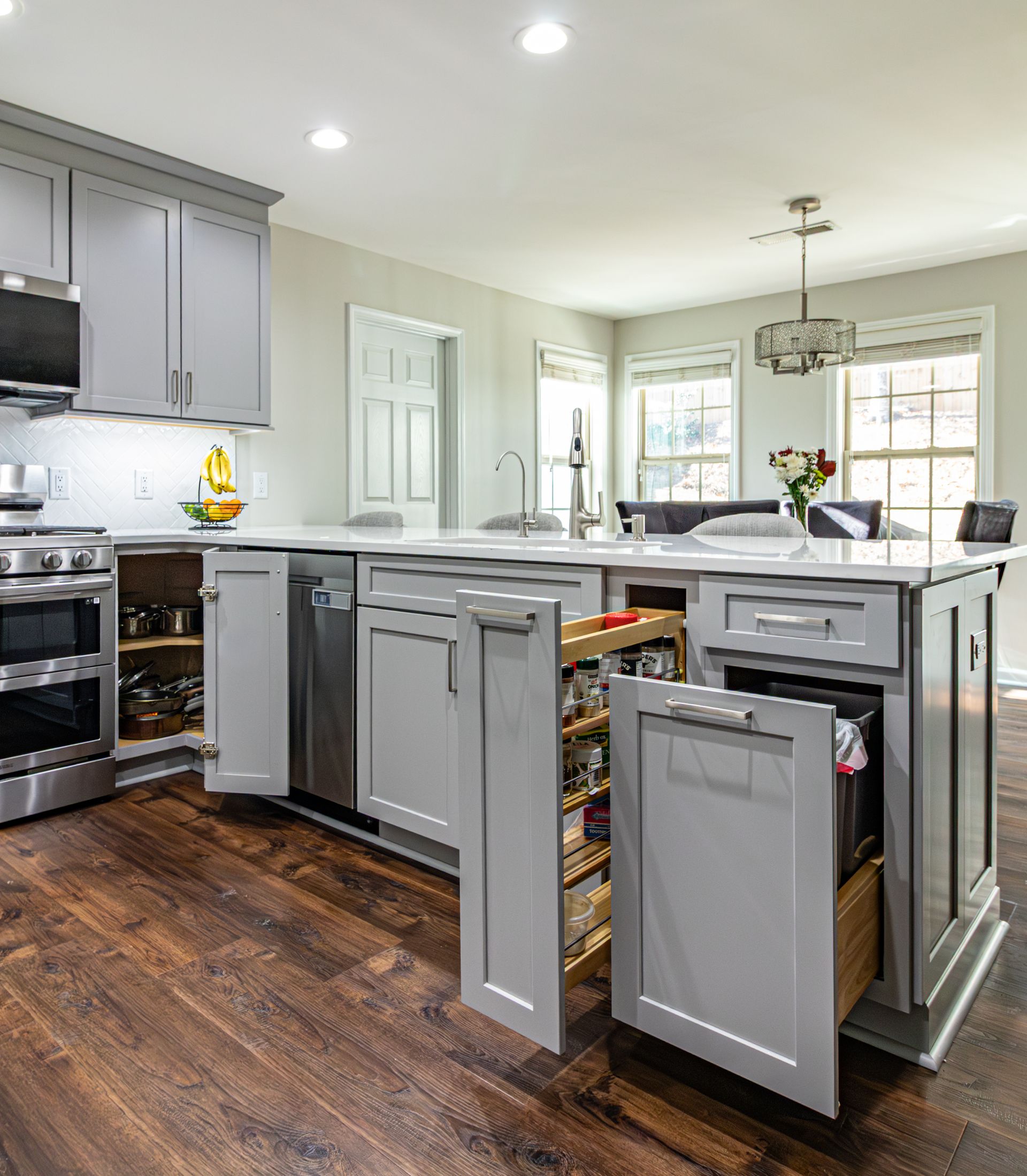 Modern kitchen with gray cabinets, stainless appliances, and a dark wood floor around a central island.