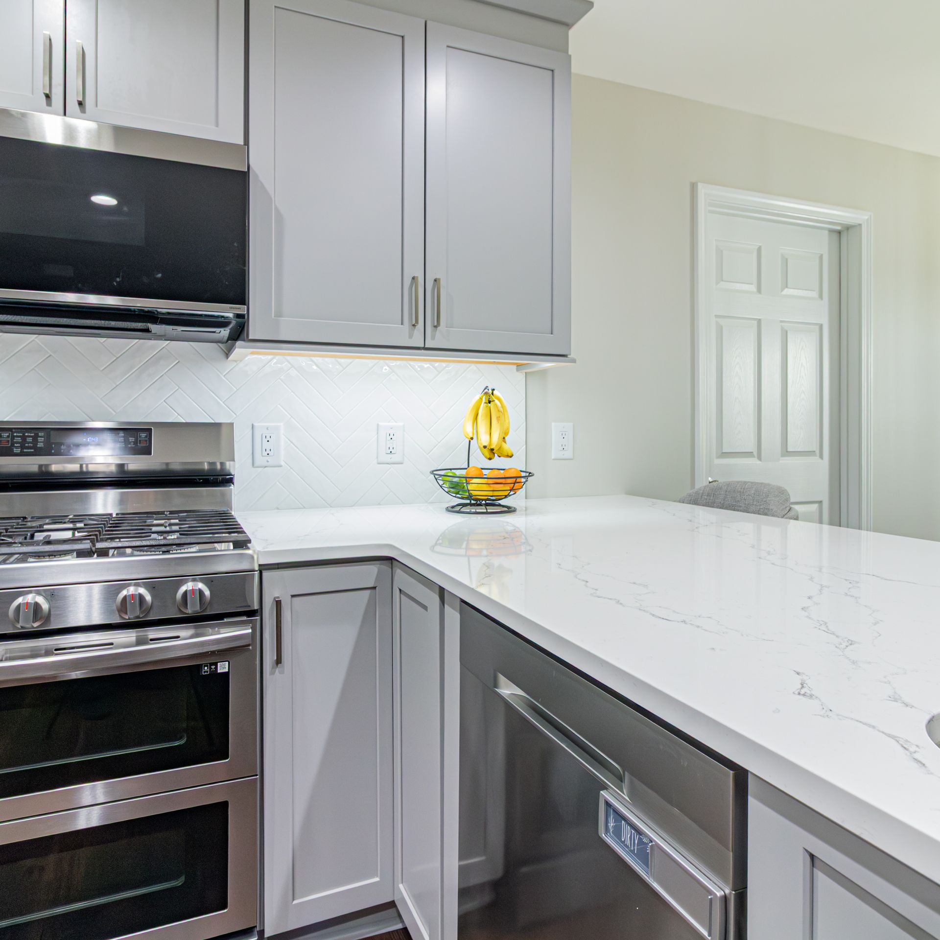 Modern kitchen with white marble countertop, gray cabinets, stainless steel appliances, and fruit bowl.