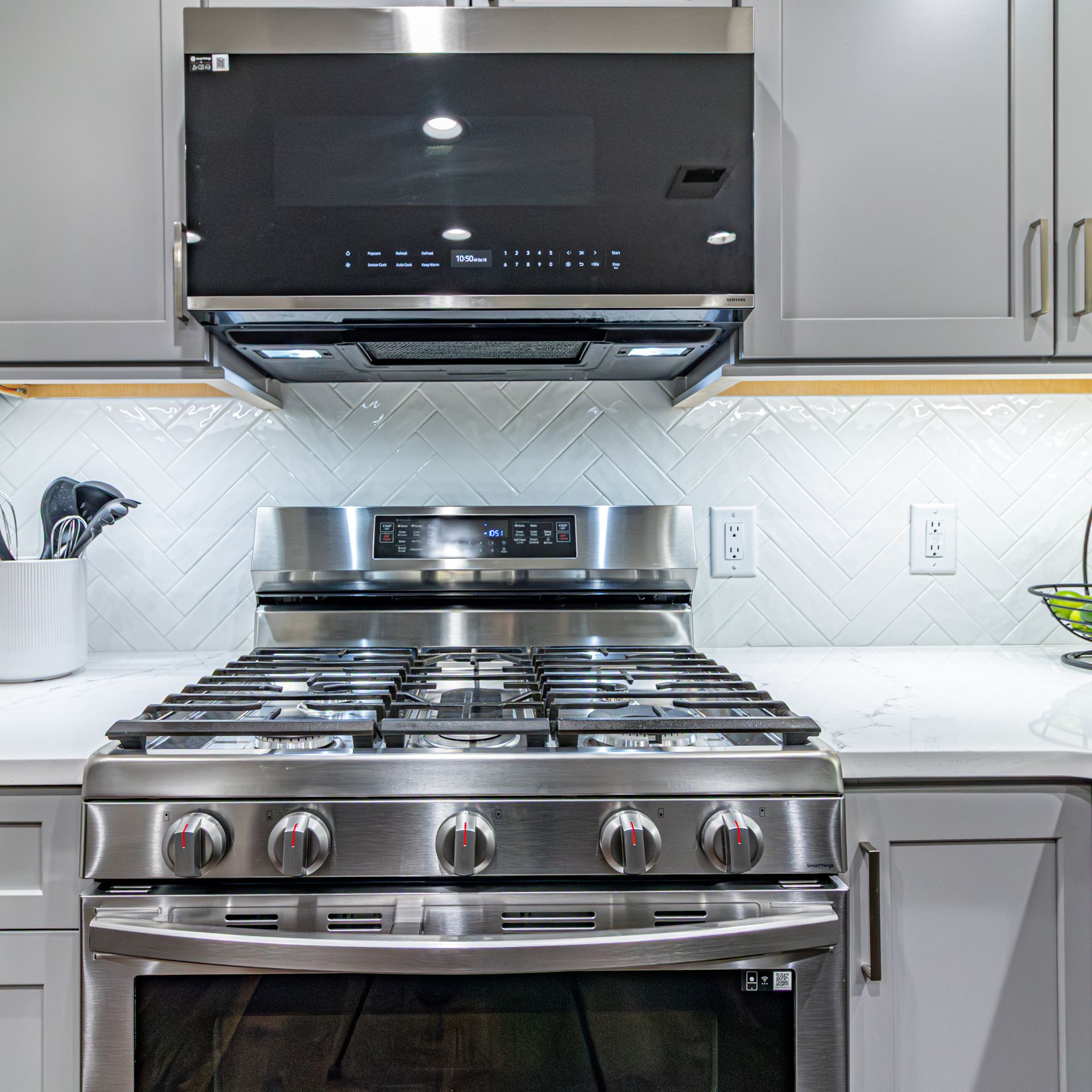 Modern kitchen with stainless steel gas range and black vent hood against gray cabinets