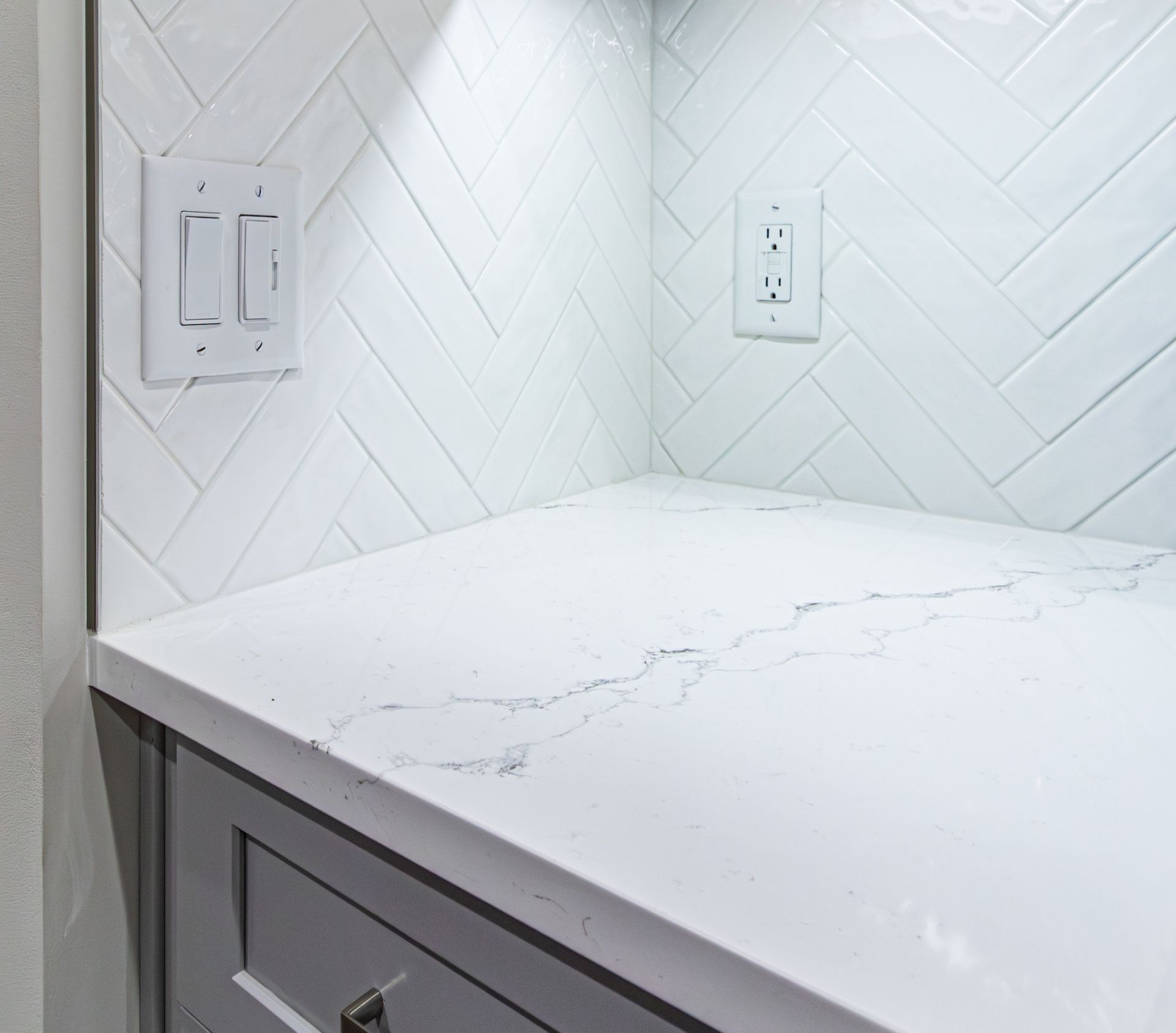 White quartz countertop with gray cabinet and herringbone tile backsplash in a kitchen nook