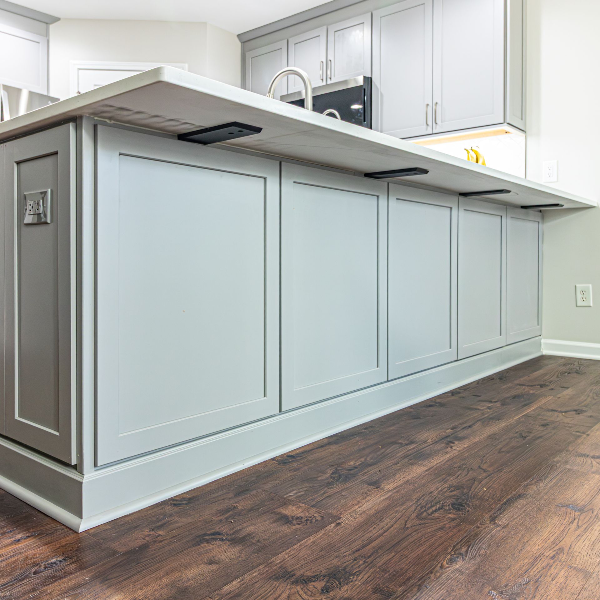 Modern kitchen island with light gray cabinets, white countertop, and wood floors