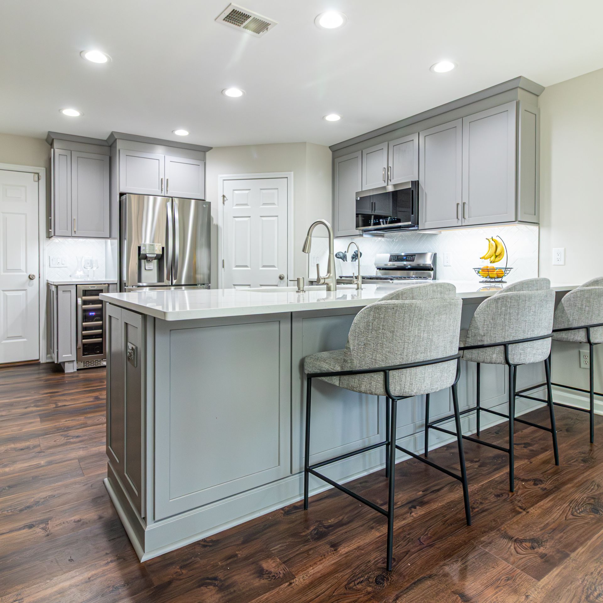 Modern gray kitchen with large island, stainless steel appliances, bar stools, and hardwood floors