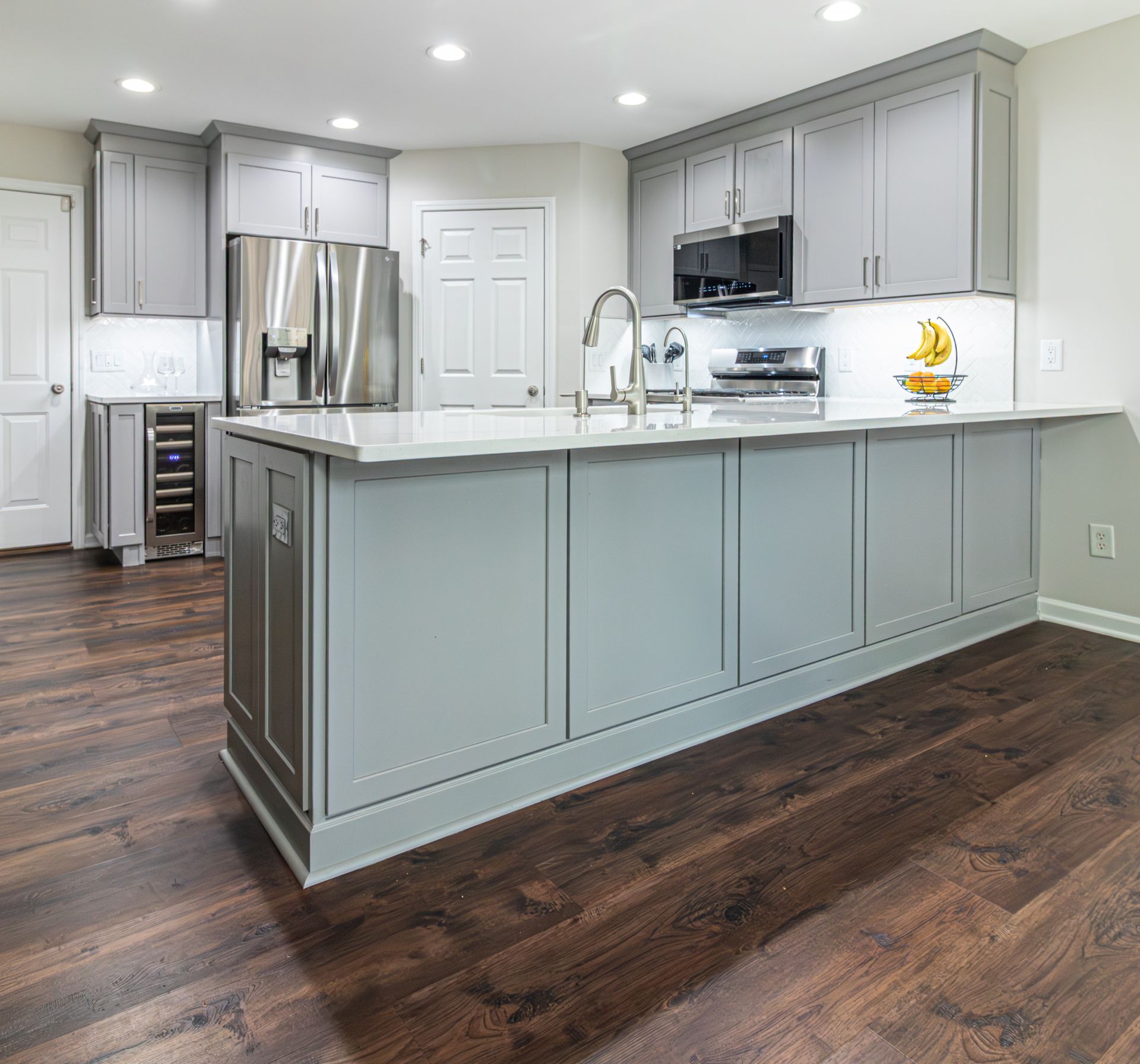 Modern kitchen with gray cabinets, stainless appliances, white countertops, and dark wood floors