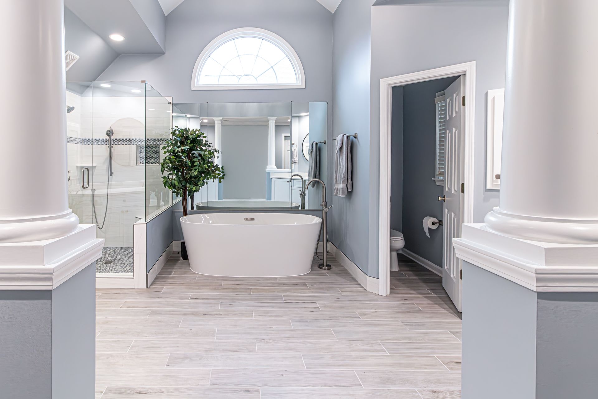 Bright modern bathroom with a freestanding tub, glass shower, and light blue-gray walls.
