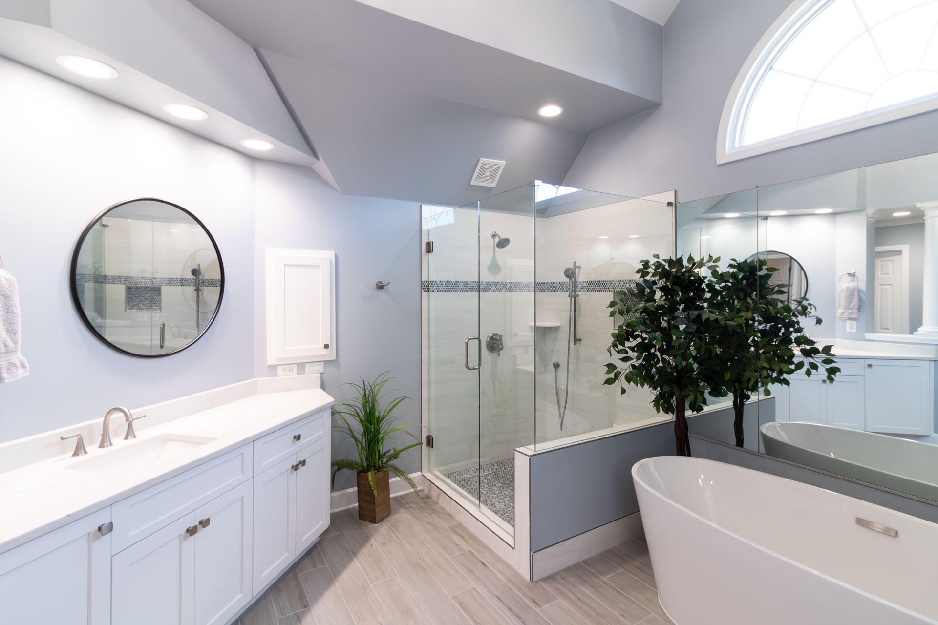 Bright modern bathroom with double vanity, glass shower, freestanding tub, and a potted tree