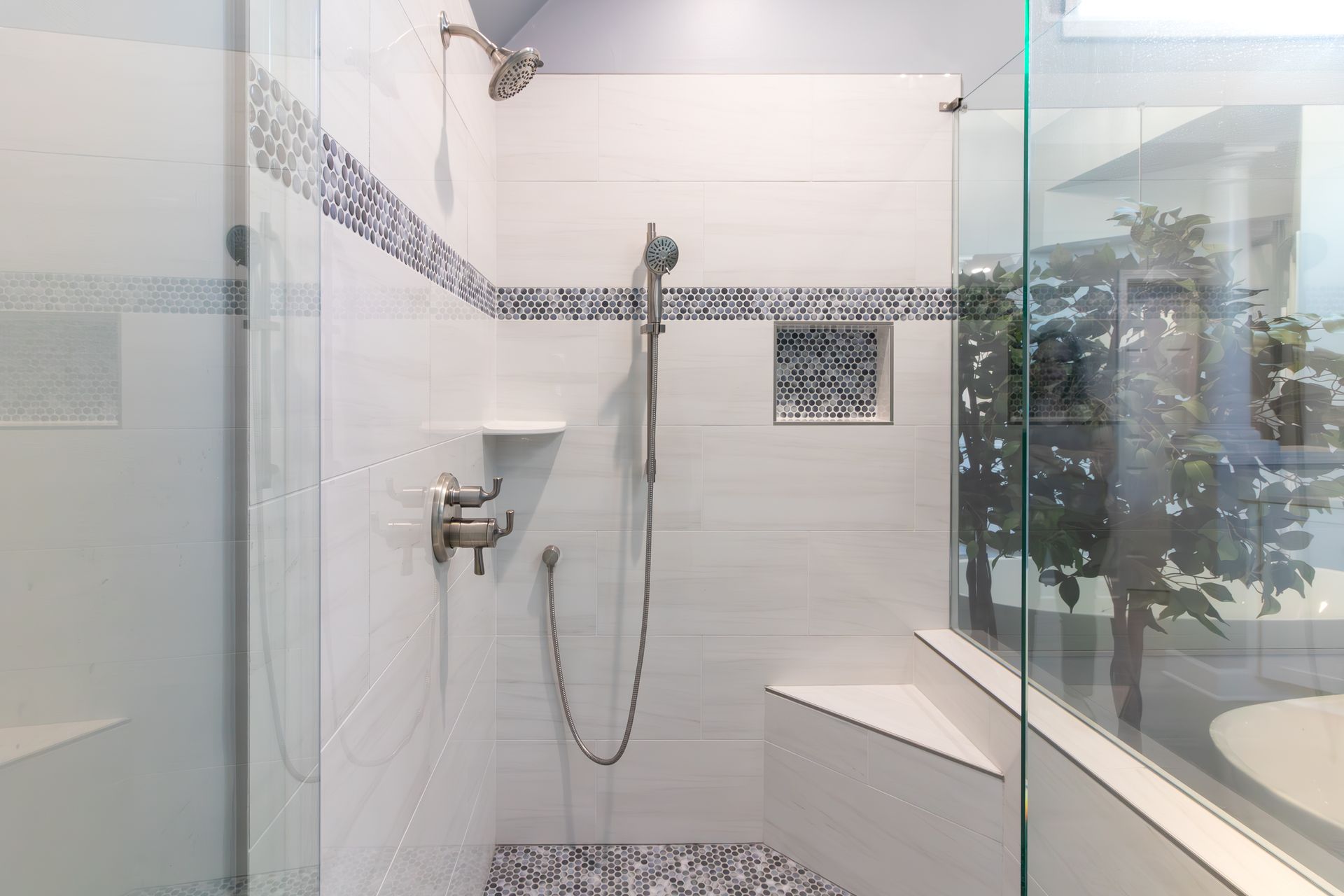 Modern white-tiled shower with glass walls, handheld showerhead, and mosaic accent tiles