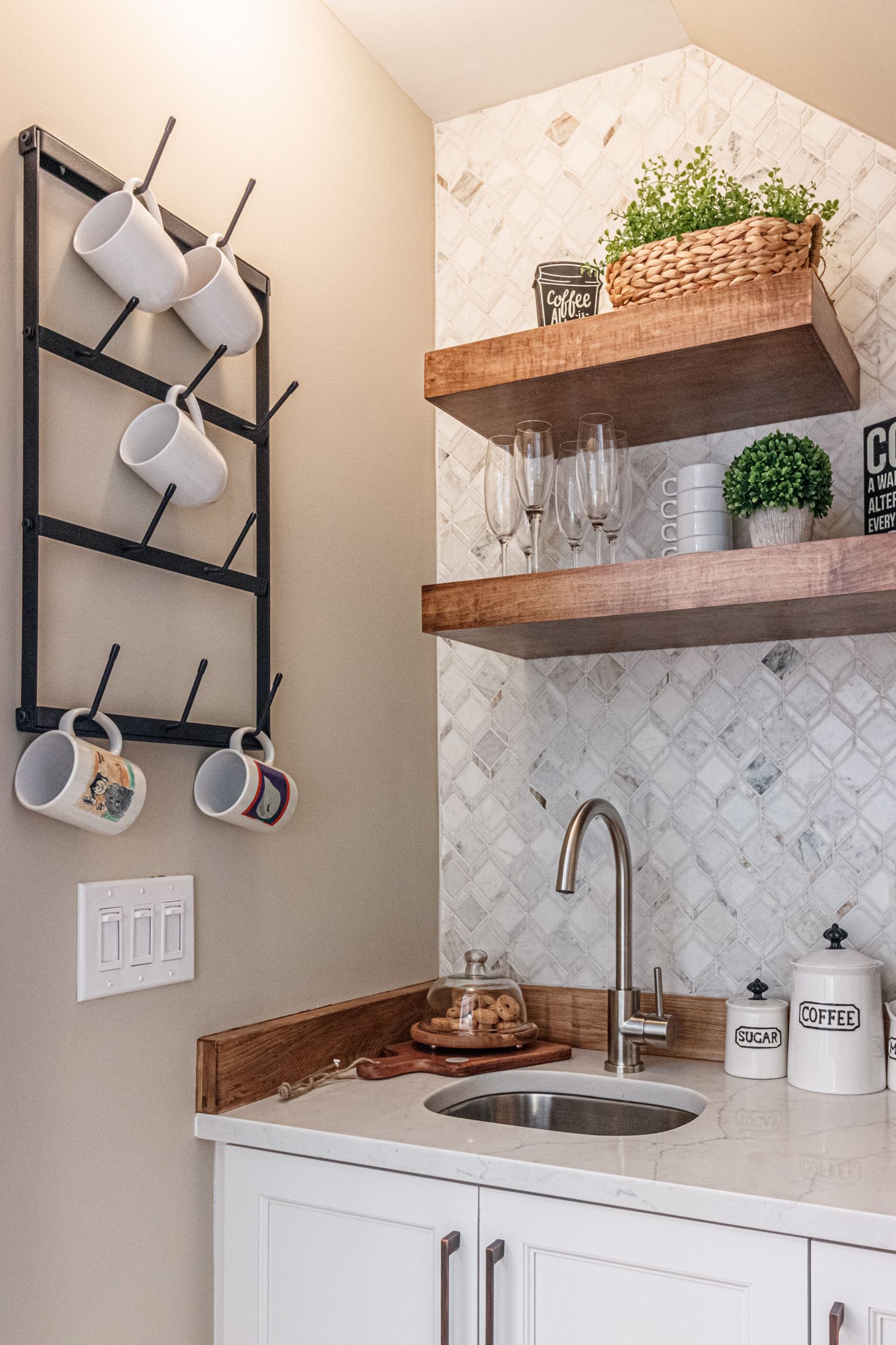 Small kitchen nook with open wood shelves, white cabinets, a sink, and hanging mugs on a wall rack.