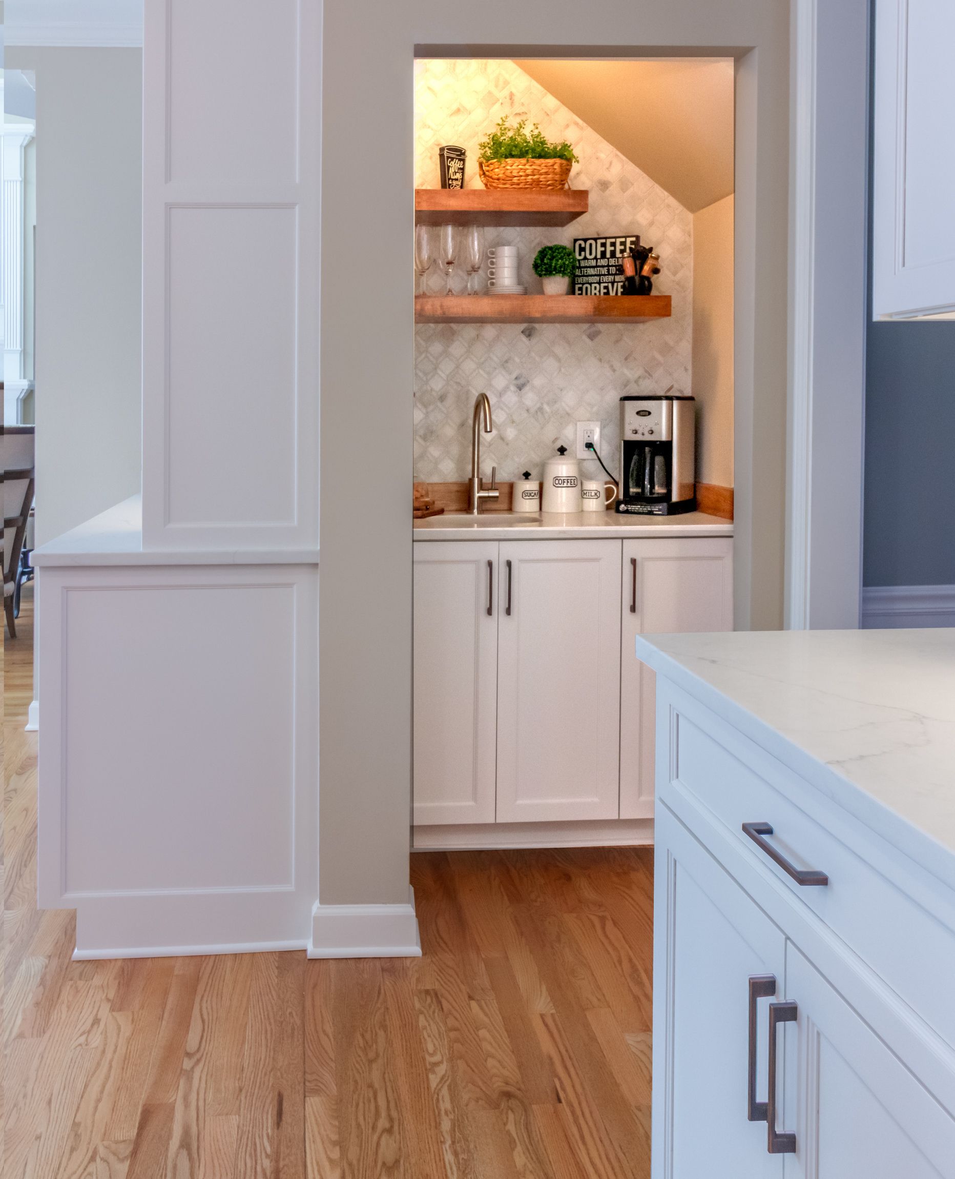 Bright kitchen alcove with white cabinets, wood shelves, coffee maker, and light wood floor.