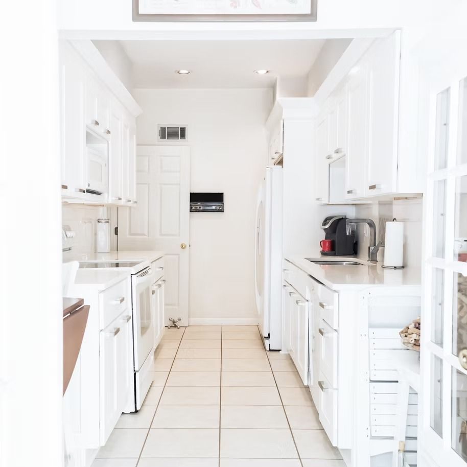 Bright white galley kitchen with tiled floor, cabinets, and small appliances along both sides