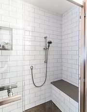 Accessible shower with white tile walls, handheld showerhead, grab bars, and built-in bench.