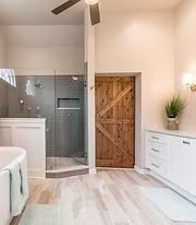 Modern bathroom with glass shower, barn-style wooden door, white vanity, and light wood floor.