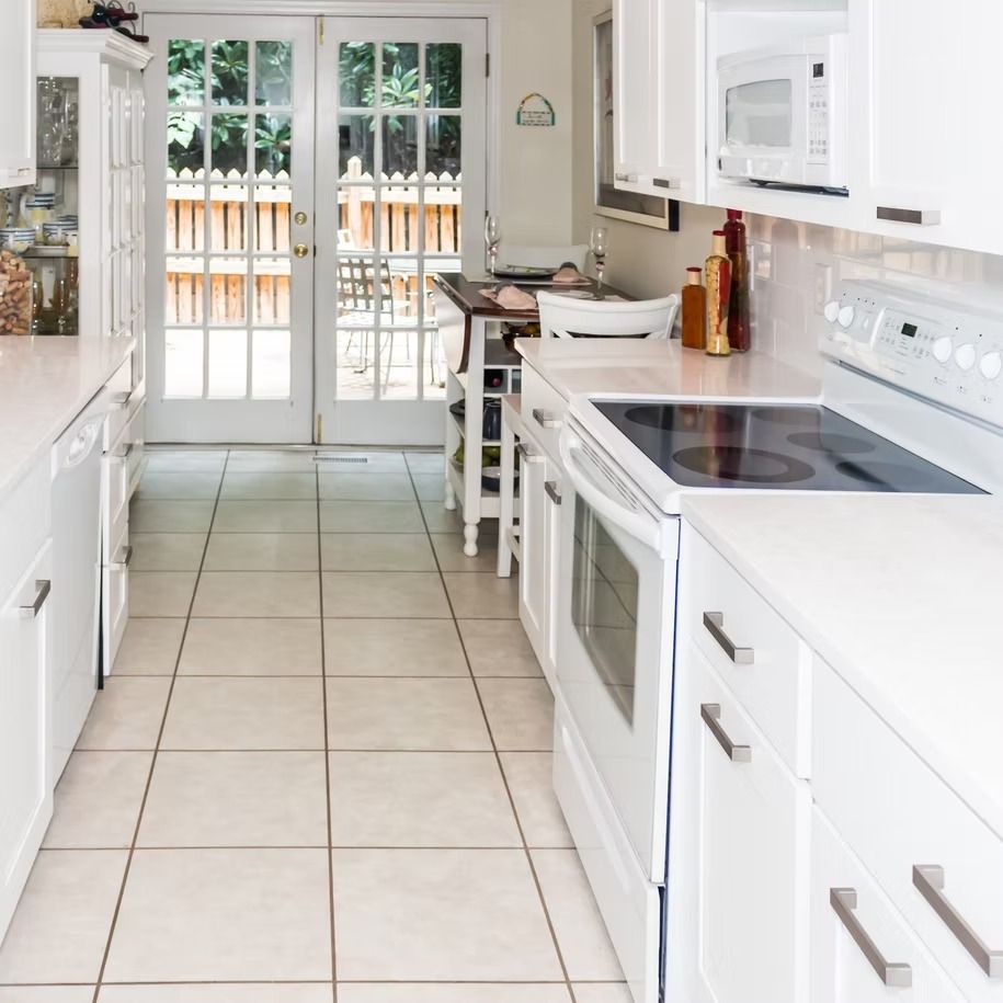 Bright white kitchen with tiled floor, electric stove, microwave, and glass doors opening to a fenced patio.
