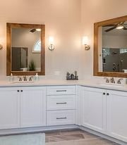 White bathroom vanity with double sinks, central drawers, large mirrors, and wall sconces.